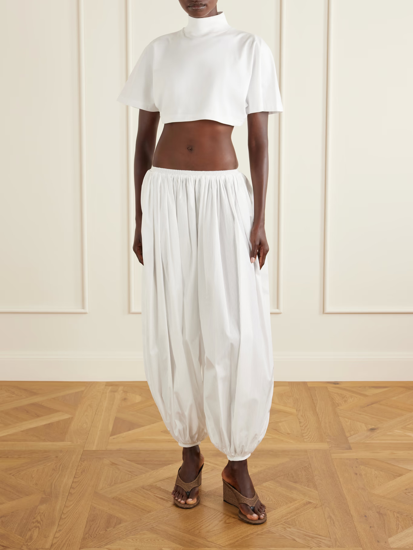 An image of a model wearing white, striped cotton poplin balloon trousers with a white mock-neck short-sleeved crop top