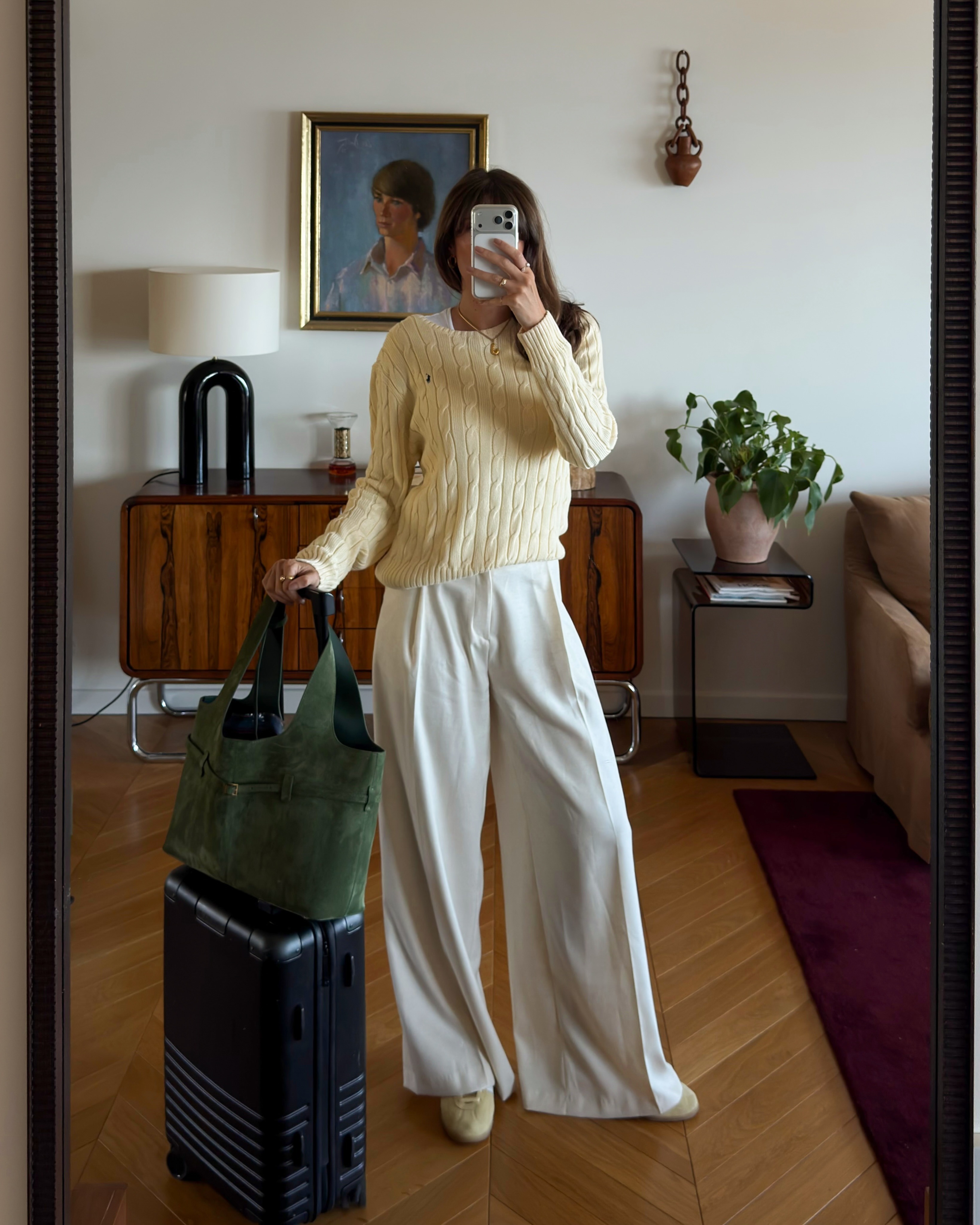 French woman wearing a travel outfit that includes a butter yellow sweater, cream trousers, and ballet flats