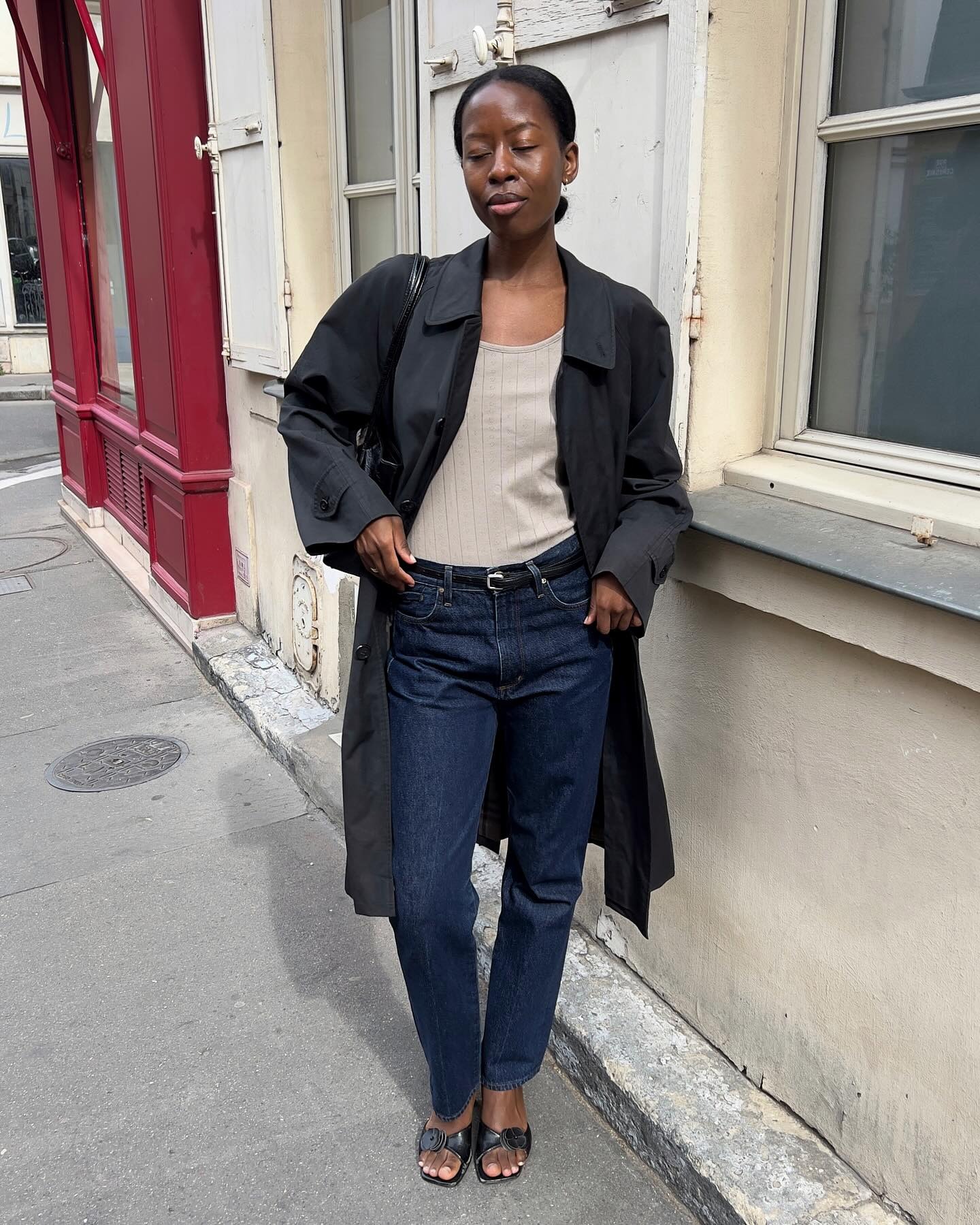 Sylvie wears black trench, beige top, dark wash denim, and black heels.