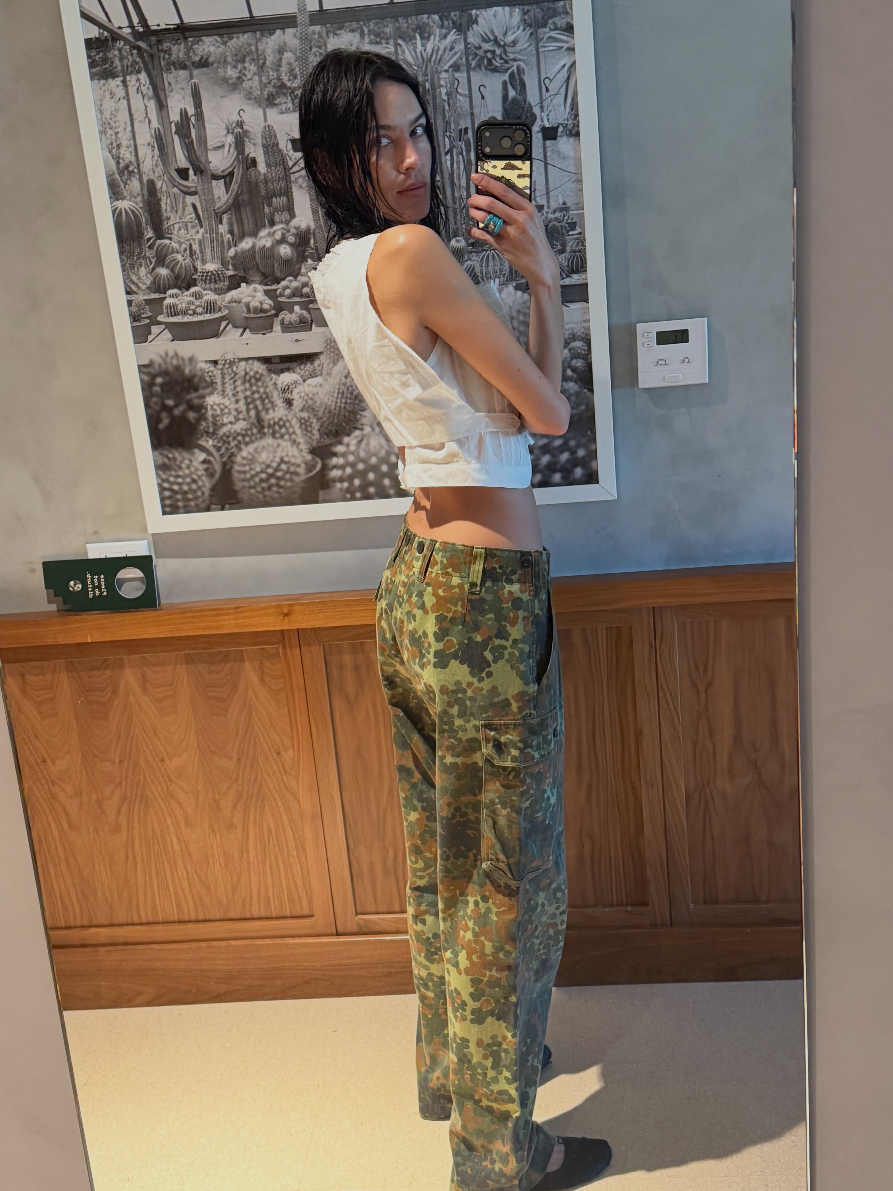 Alexa Chung takes a mirror selfie wearing camo trousers with a white cropped top.