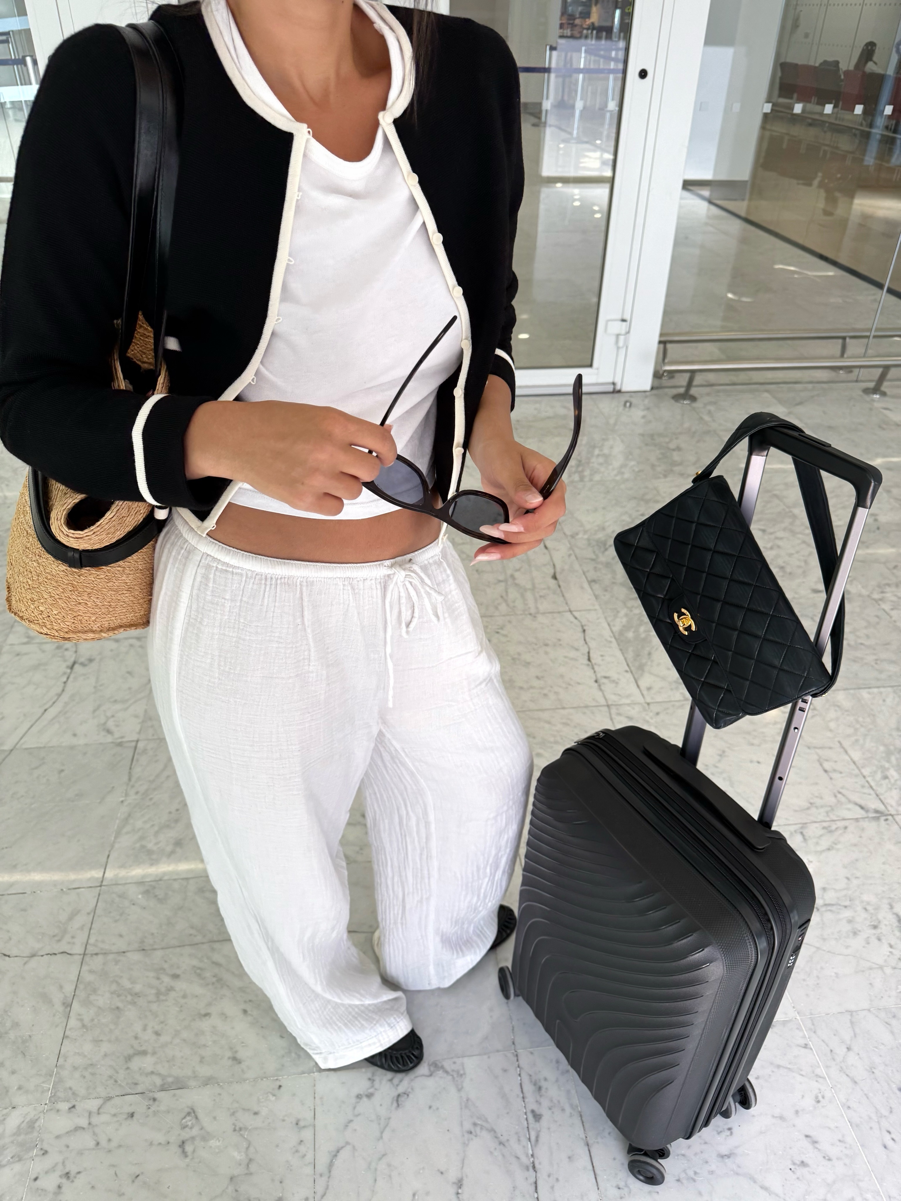 French woman wearing a travel outfit that includes a black-and-white tipped cardigan over a white cropped tee and pull-on pants with black leather loafers
