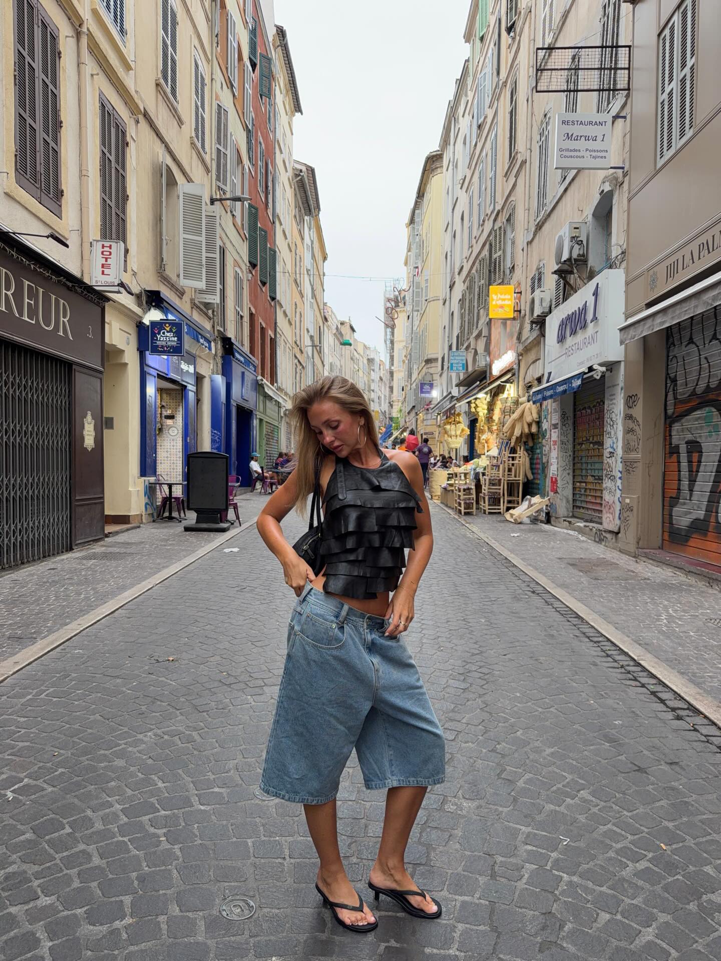 An image of @edenharper wearing long denim shorts with a halterneck top and heeled flip-flops.