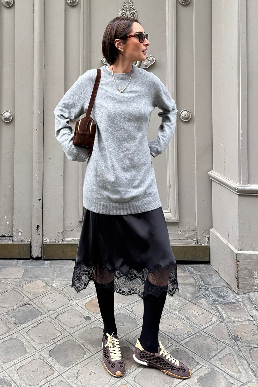 a woman wearing a gray sweater, black lace-trim skirt, and sneakers