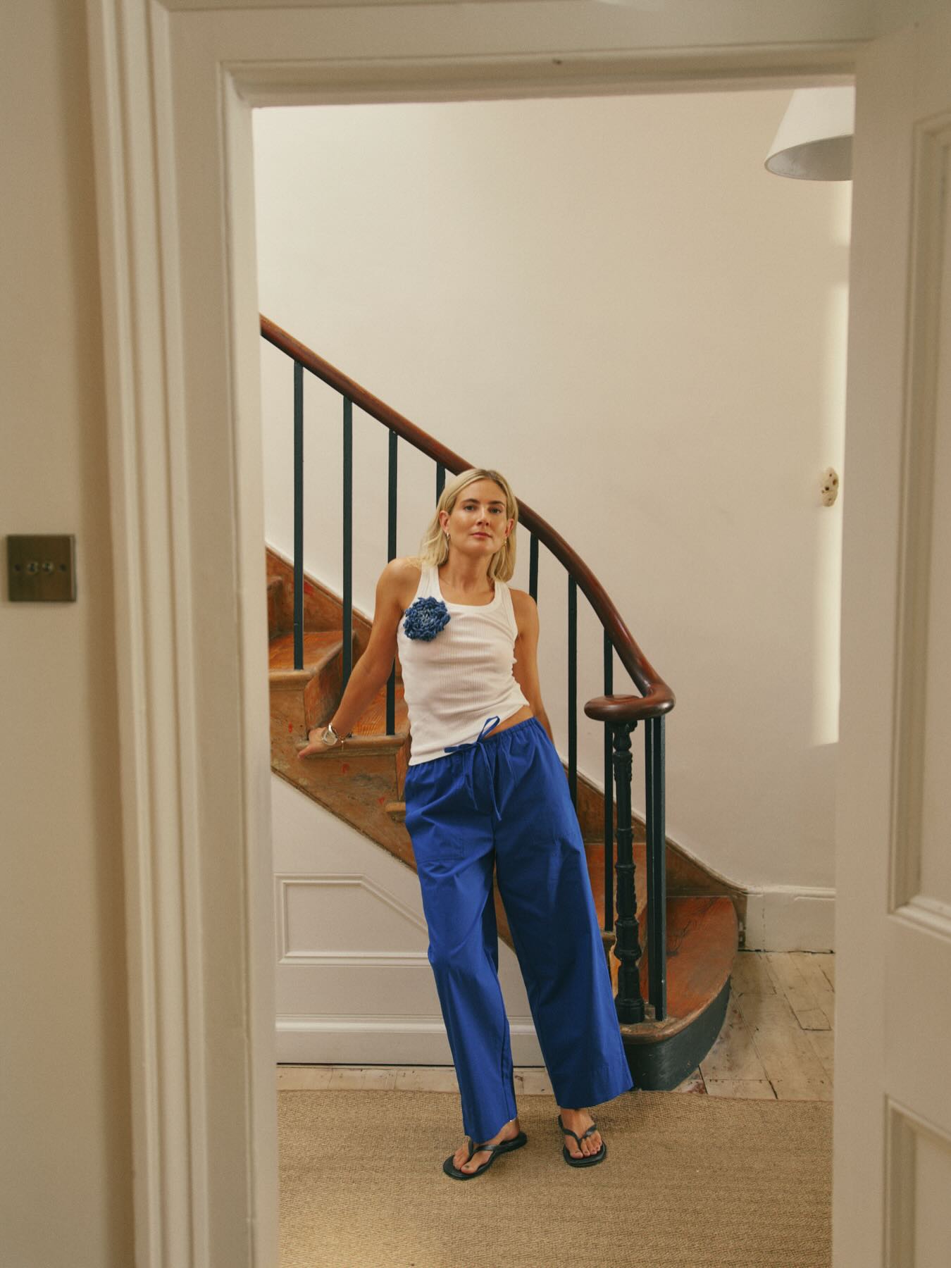 Influencer Lucy Williams wearing cobalt blue cotton drawstring trousers with a white vest top, flower brooch and flip flops.