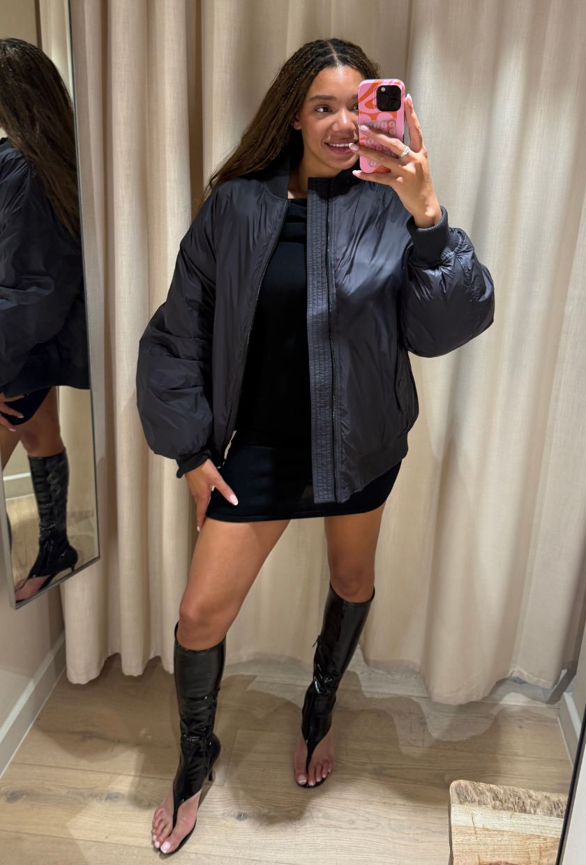 Imani wears a bomber jacket, black dress, black boots