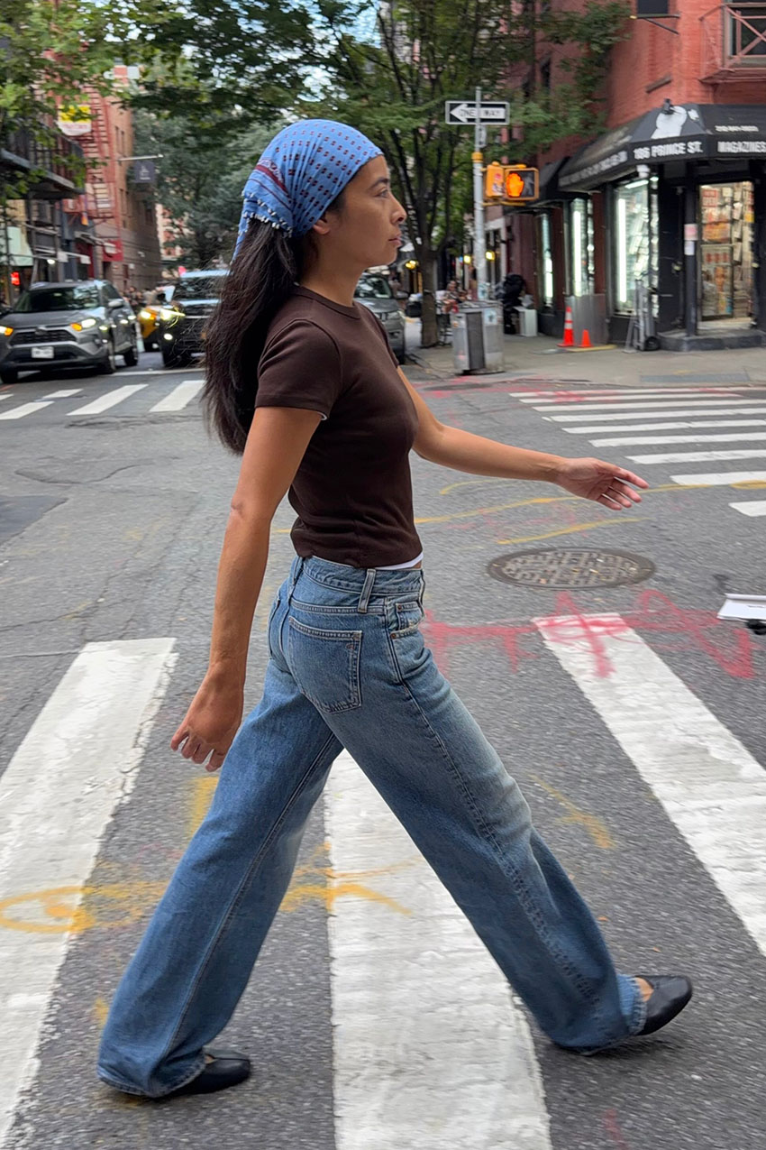 A woman wearing a blue headscarf, brown t-shirt, blue jeans, and ballet flats.