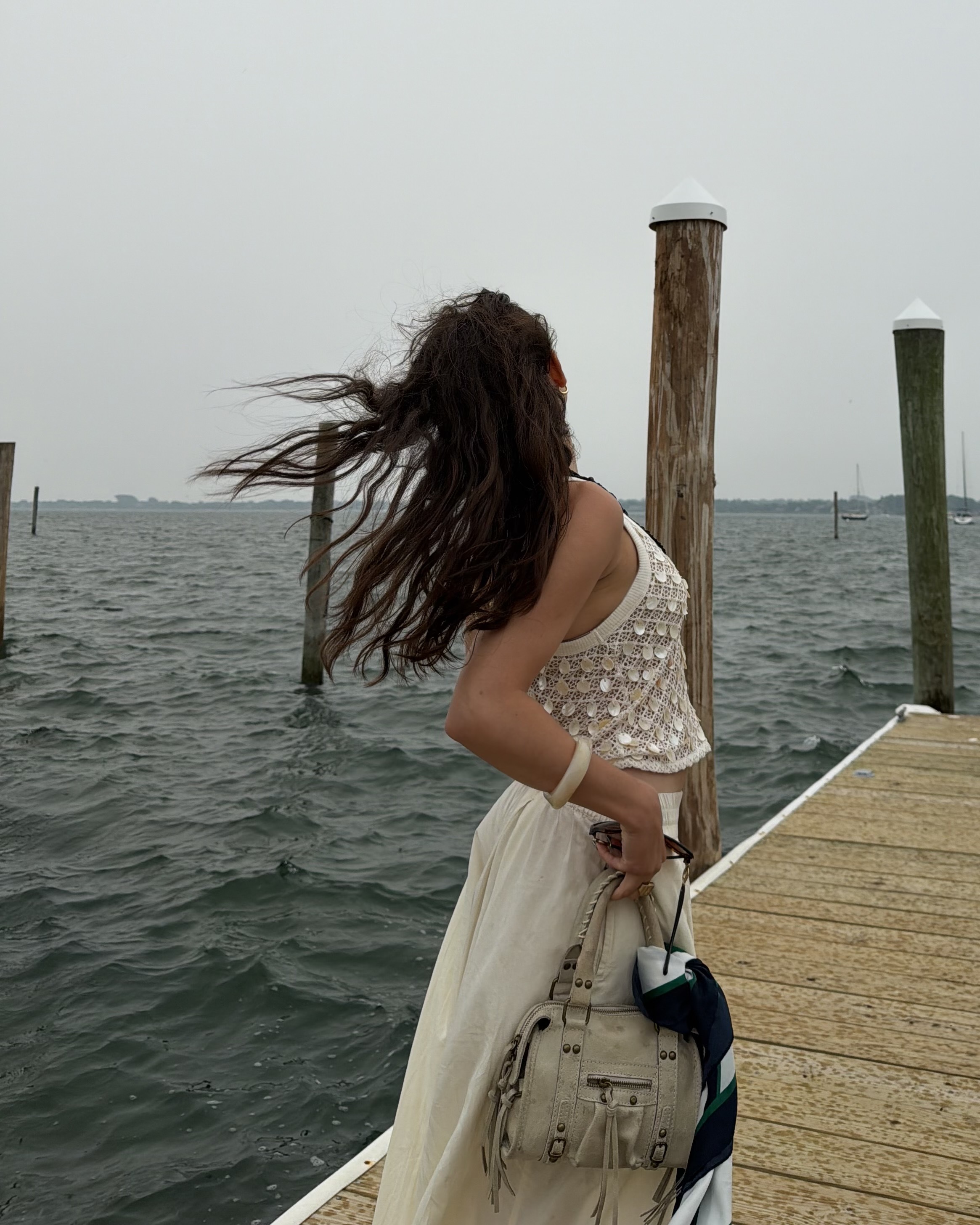 An image of Who What Wear associate beauty editor Alyssa Brascia with long, wavy brown hair blowing in the wind on a dock.