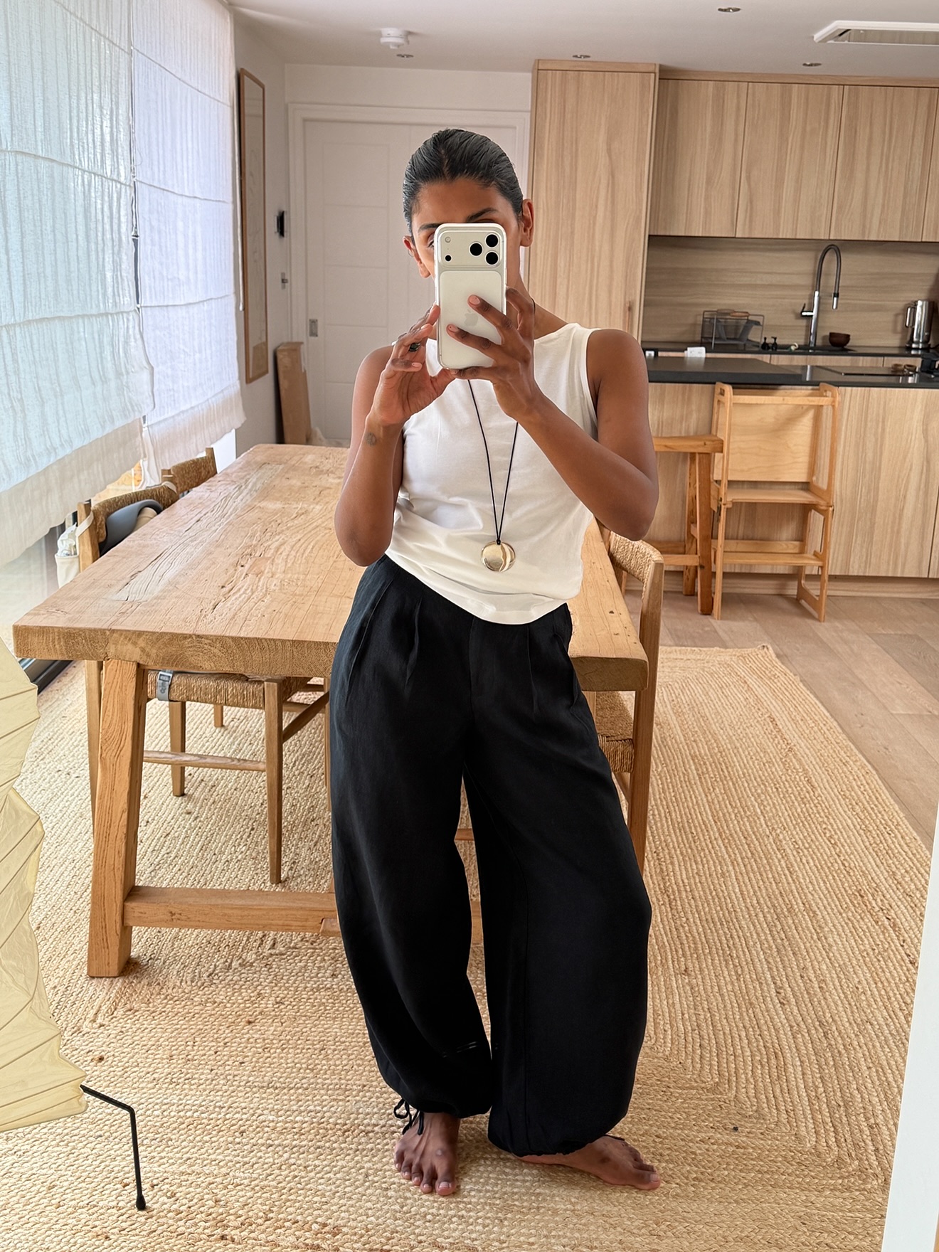 Influencer Monikh wearinh black sarouel trousers with a white tank top and cord pendant necklace.