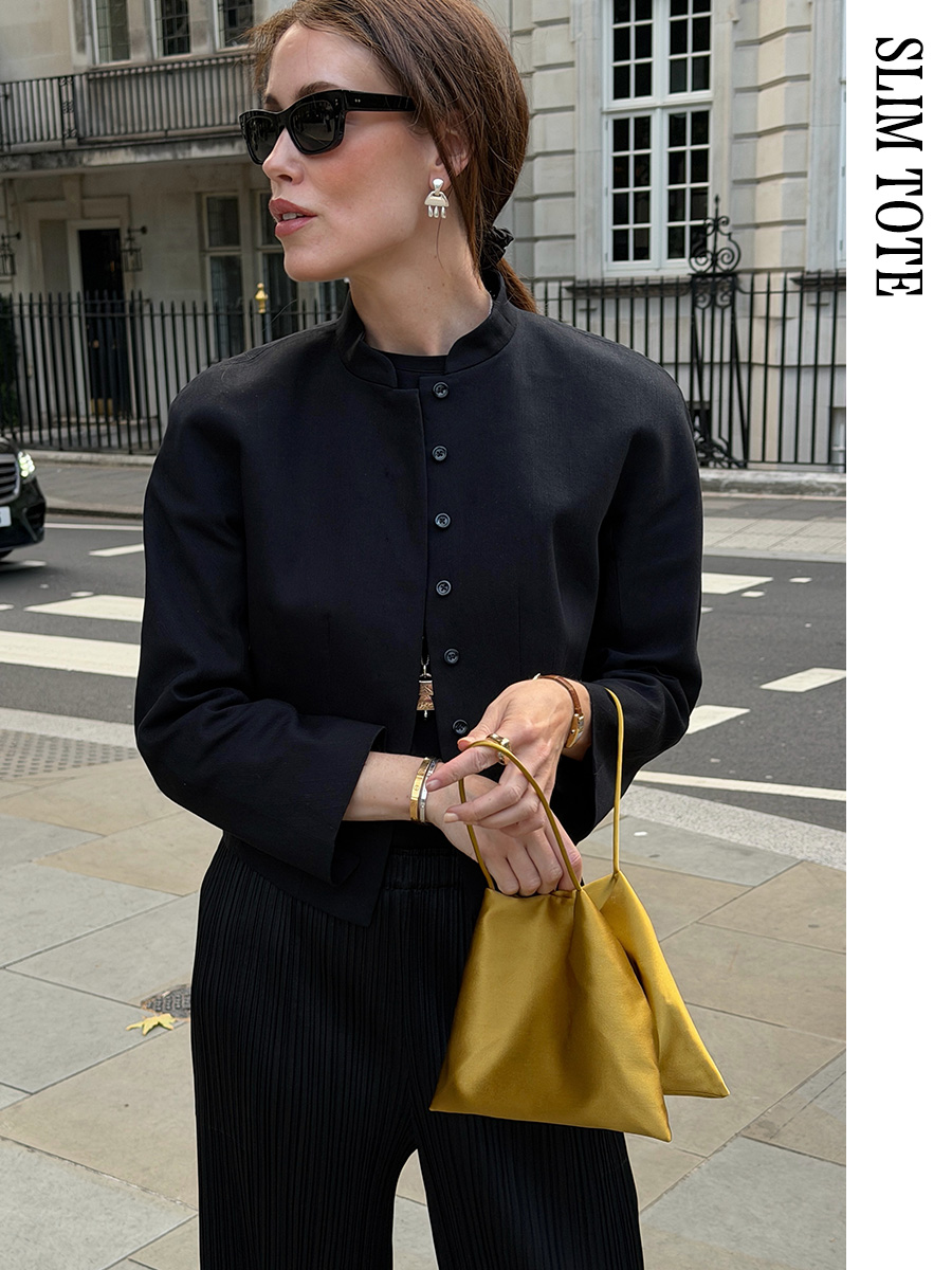 Woman wearing a black blazer, black pants, and a gold The Row Cecily bag