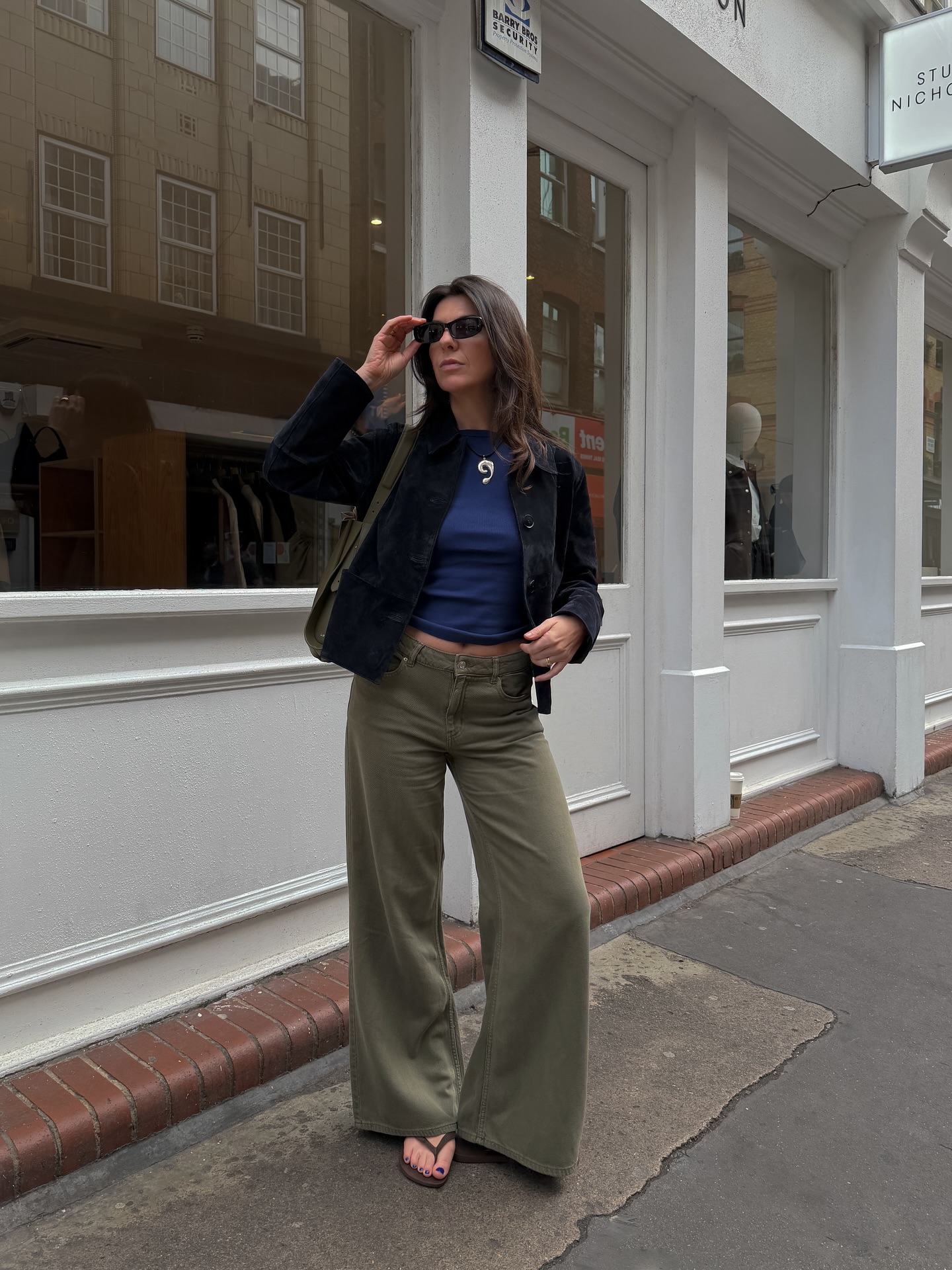 Influencer Francesca Saffari wearing a black denim jacket, blue cropped t-shirt, khaki wide-leg jeans and flip flops.