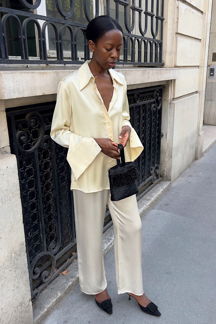 a woman wearing a creme silk shirt and pants, and black mules
