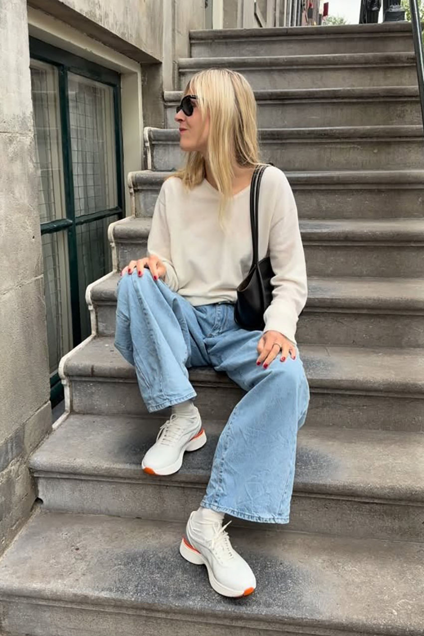 a woman wearing a cream sweater, blue jeans, and chunky sneakers