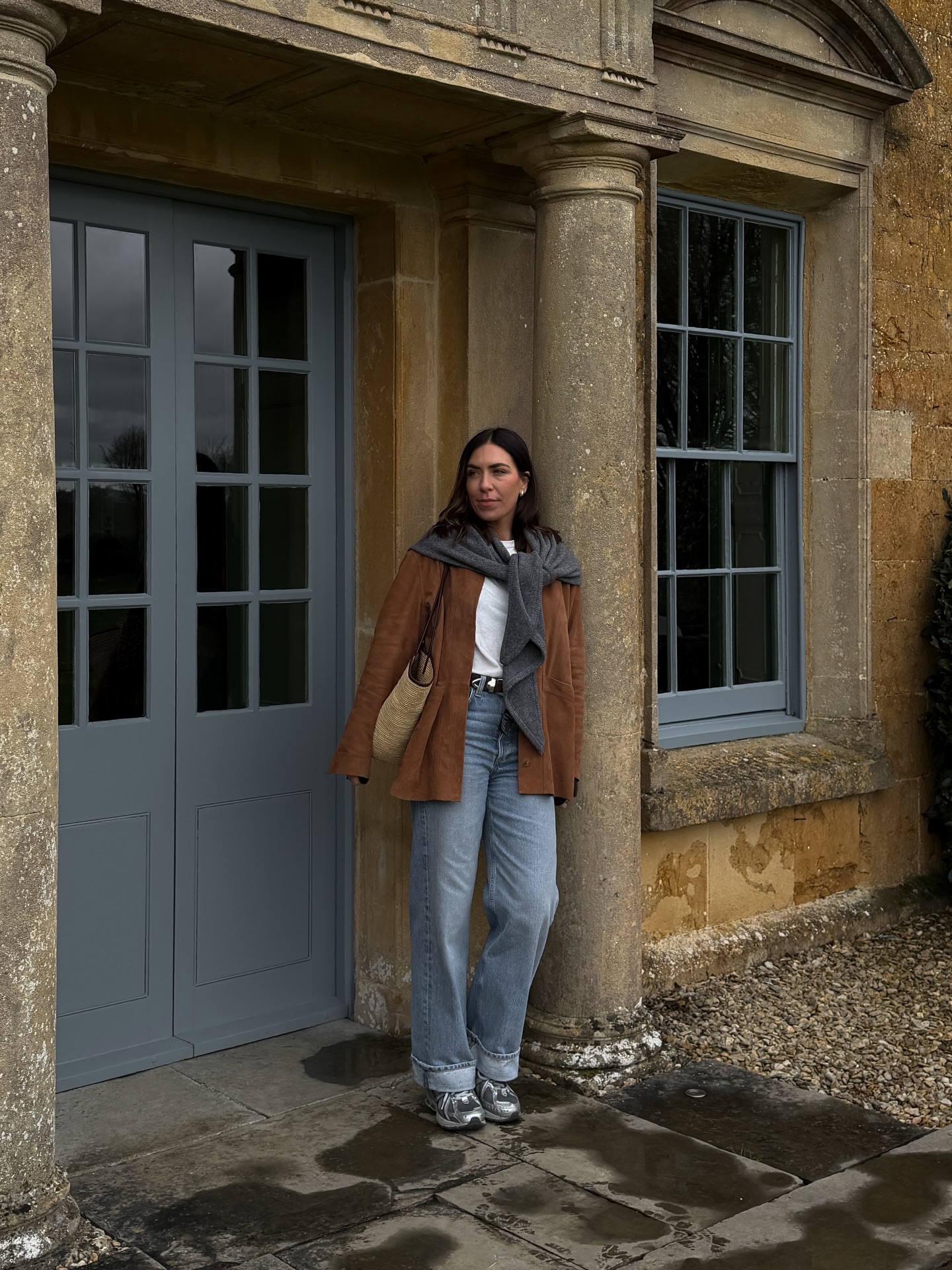 An image of an influencer wearing a brown jacket, white T-shirt, light blue jeans and silver trainers