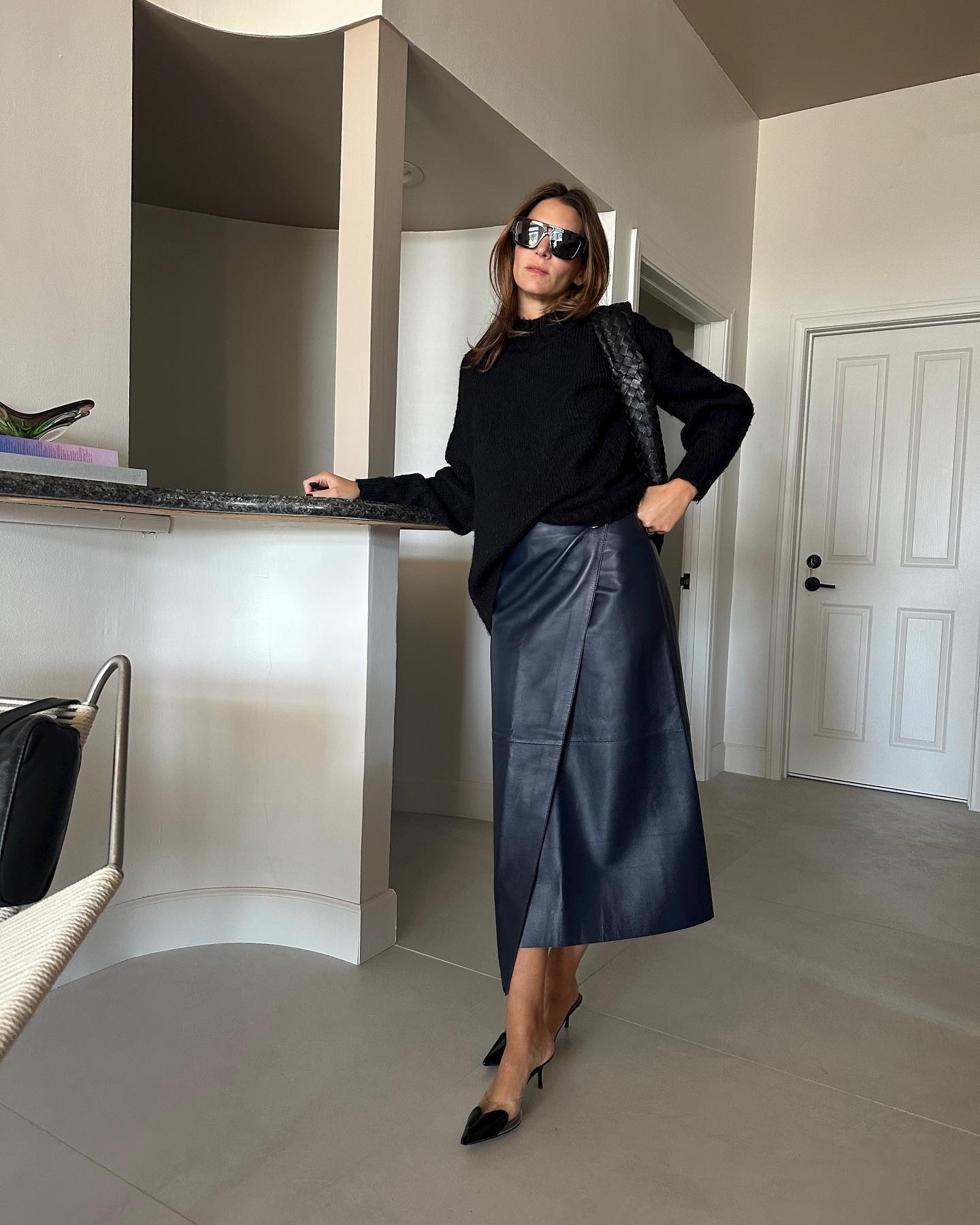 Jen Wonders in a black sweater, leather wrap skirt, and black heels.