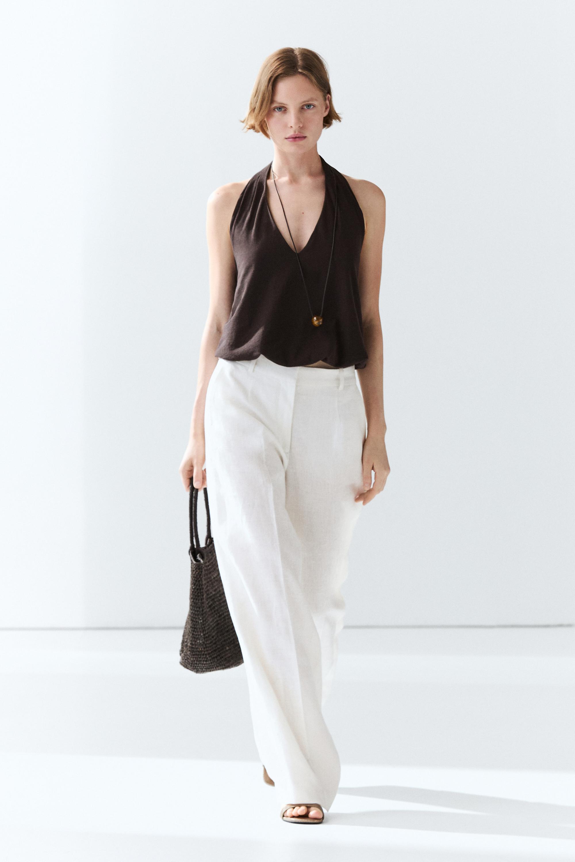An image of a model wearing white pleated linen trousers and a brown sleeveless top