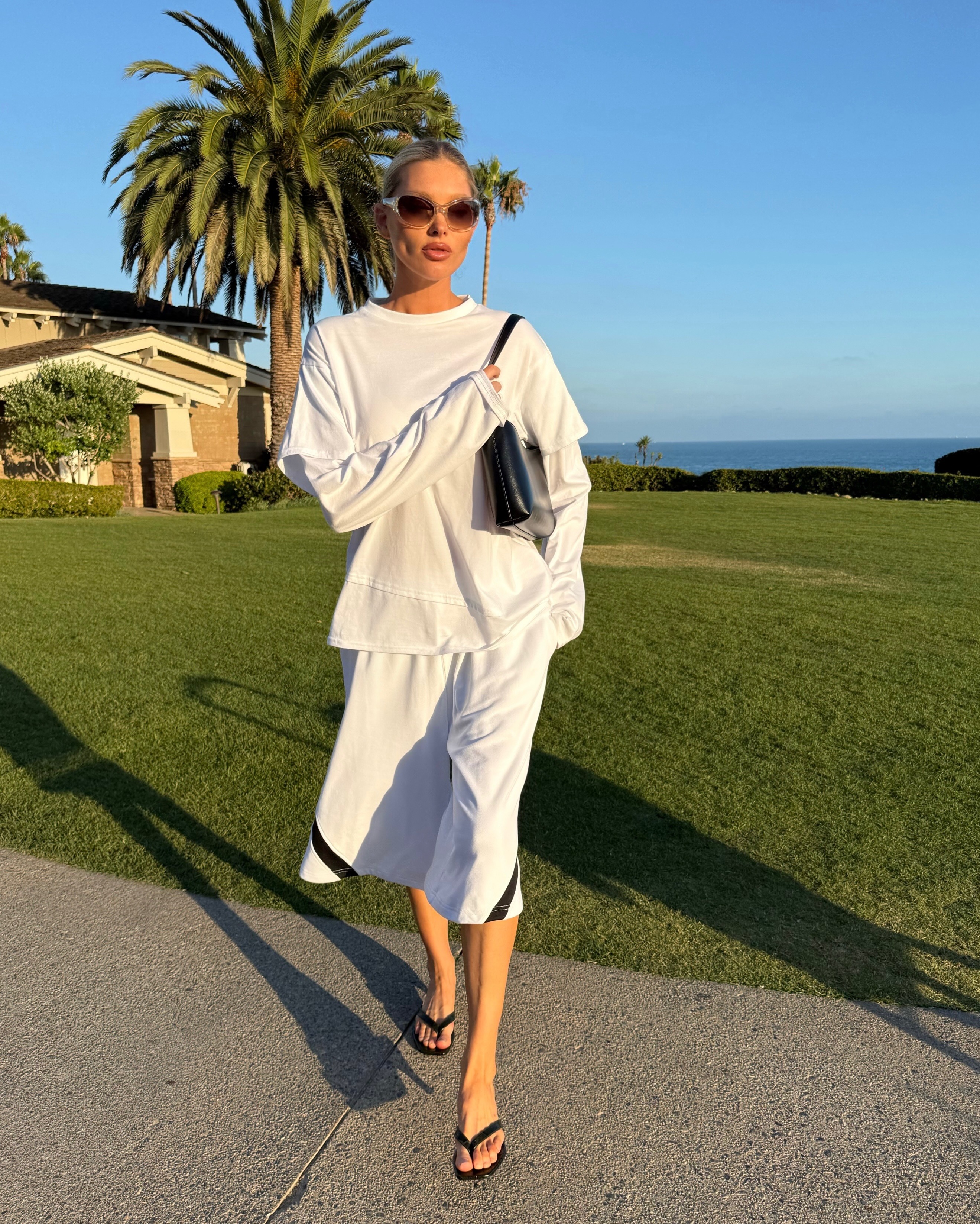 Model @hoskelsa wears longline shorts with a white long-sleeve top and black flip-flops.