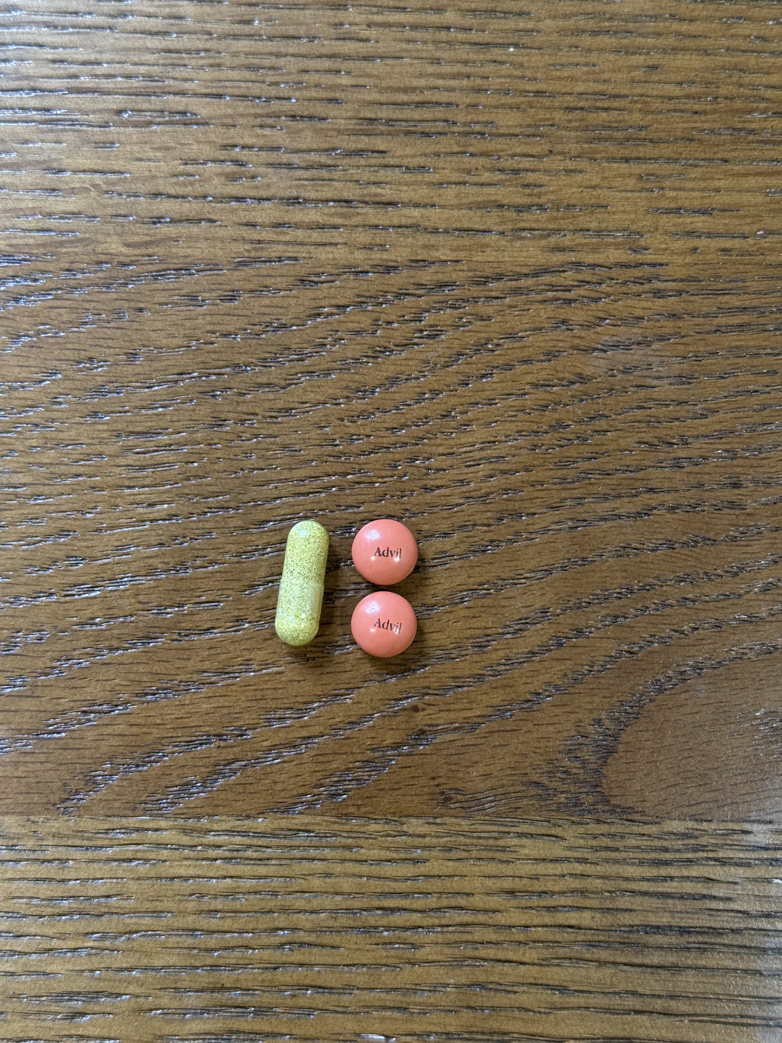 Nutrafol capsule next to two Advil tablets on a table.