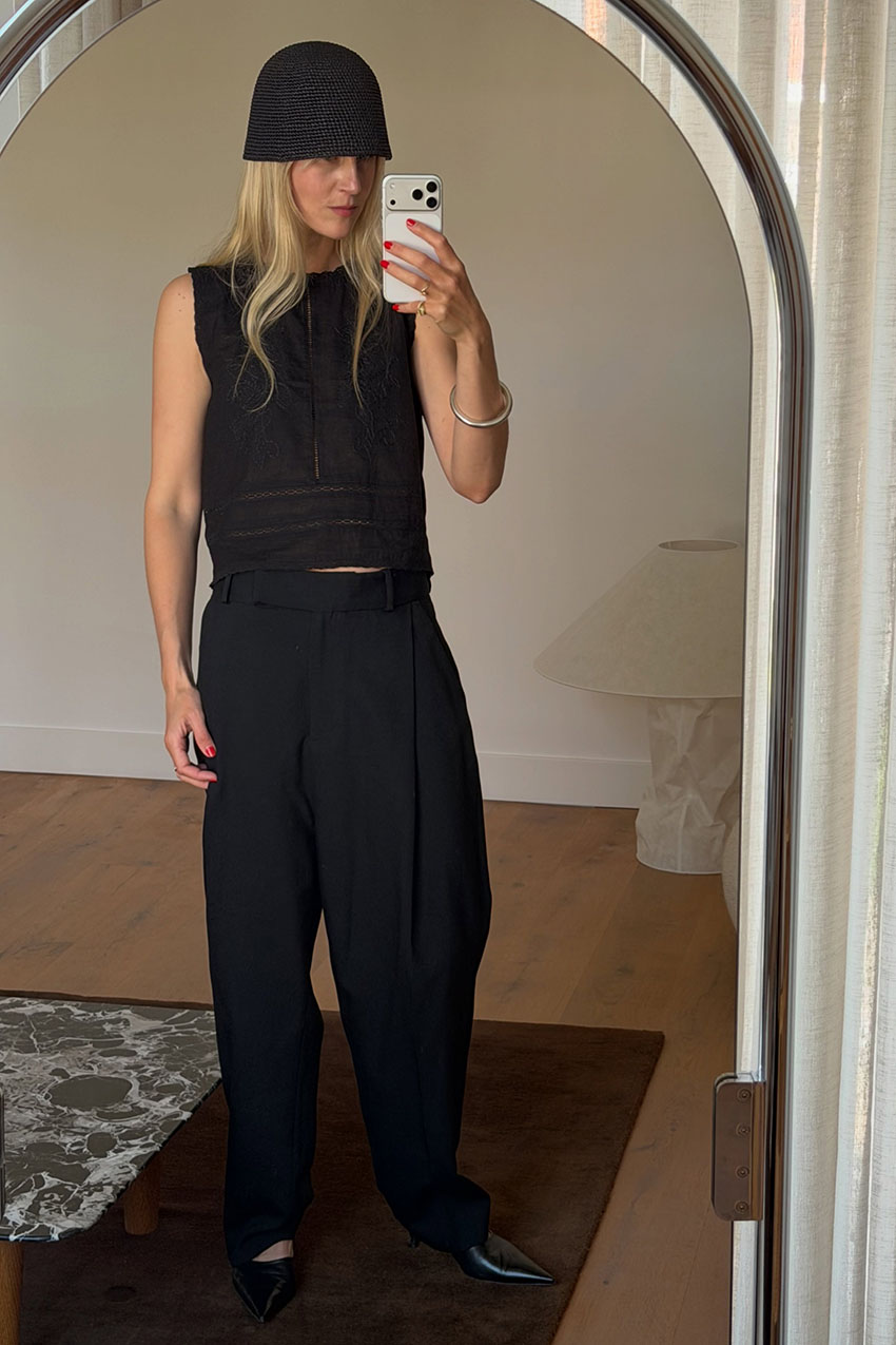 a woman wearing a black hat, black tank top, black trousers, and black pointed-toe shoes