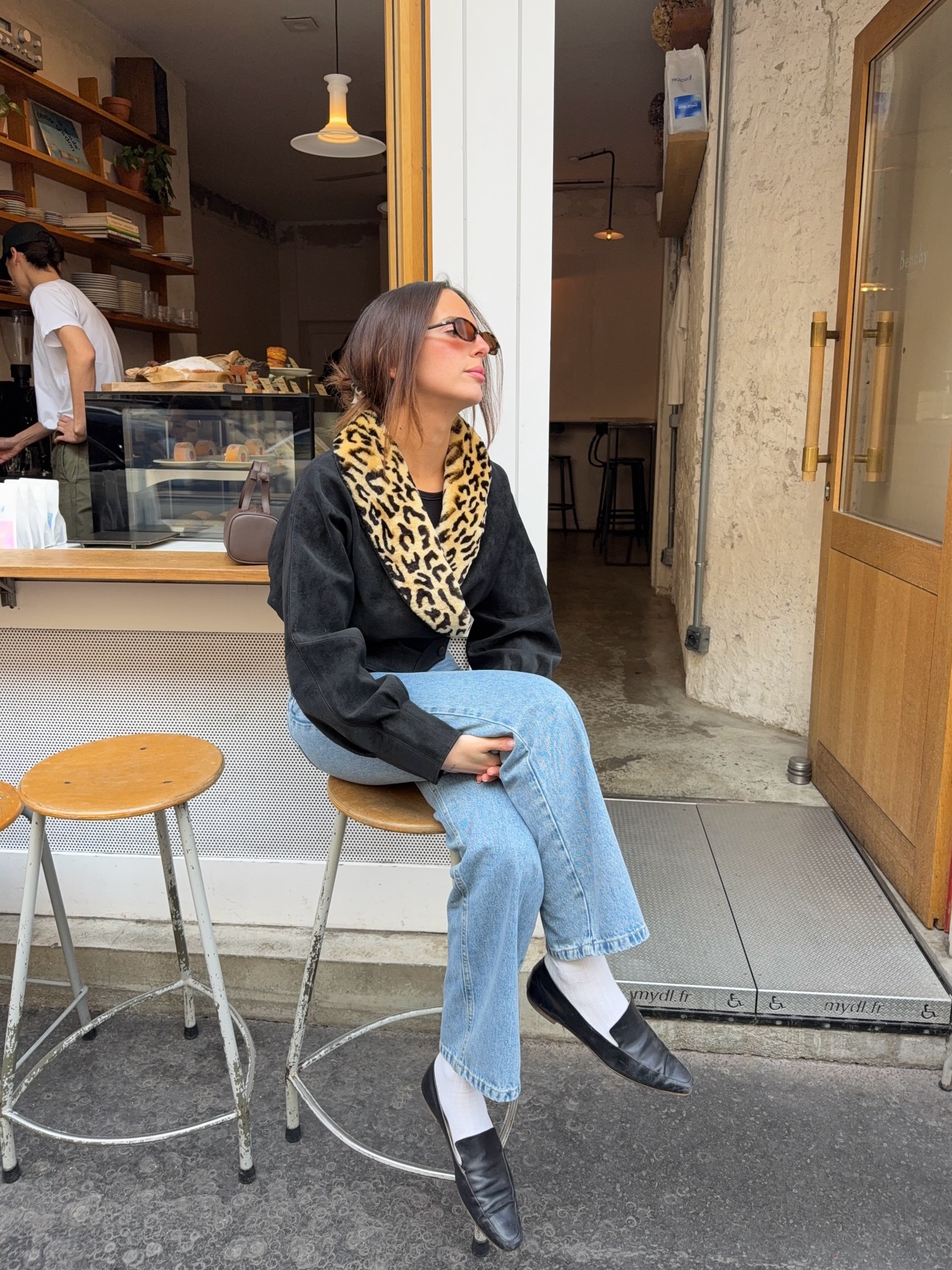 An image of an influencer wearing a black jacket with a leopard collar, light blue jeans, white socks and black loafers in Paris
