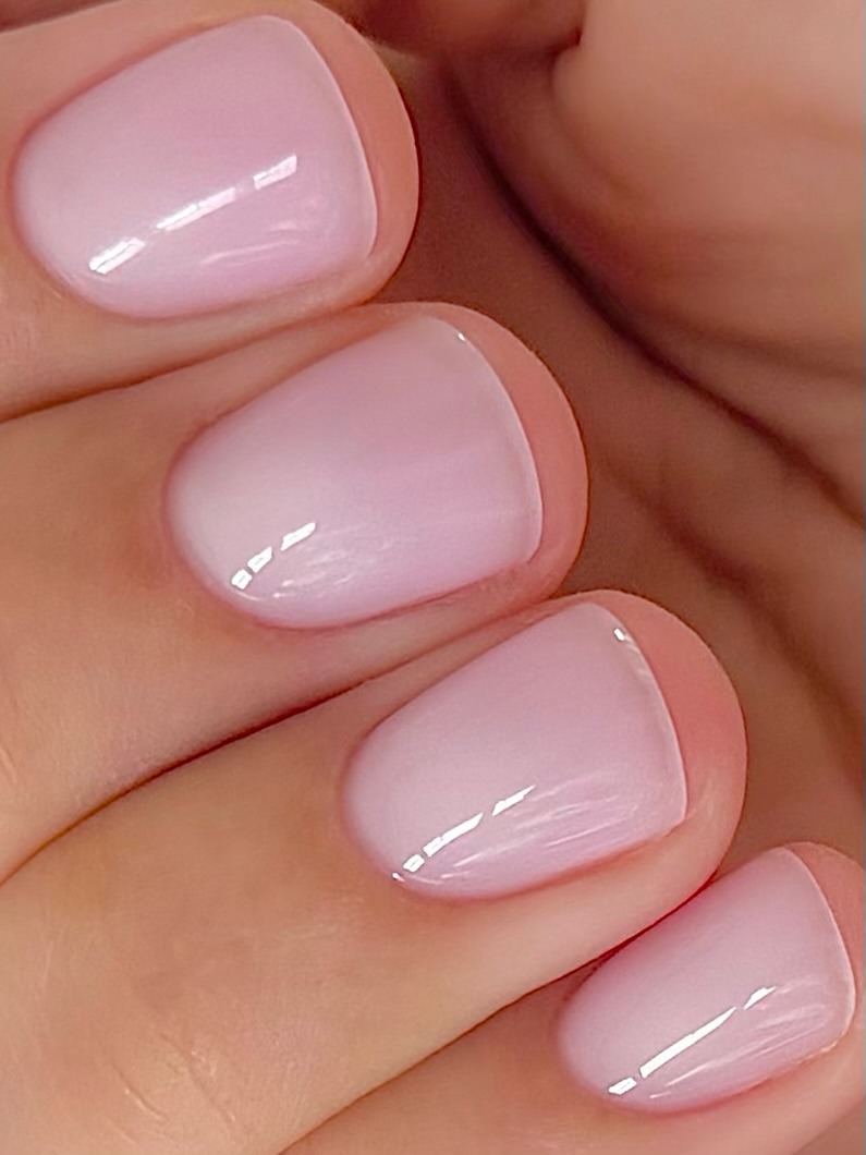 A close-up picture of a sheer, glossy, soft pink manicure