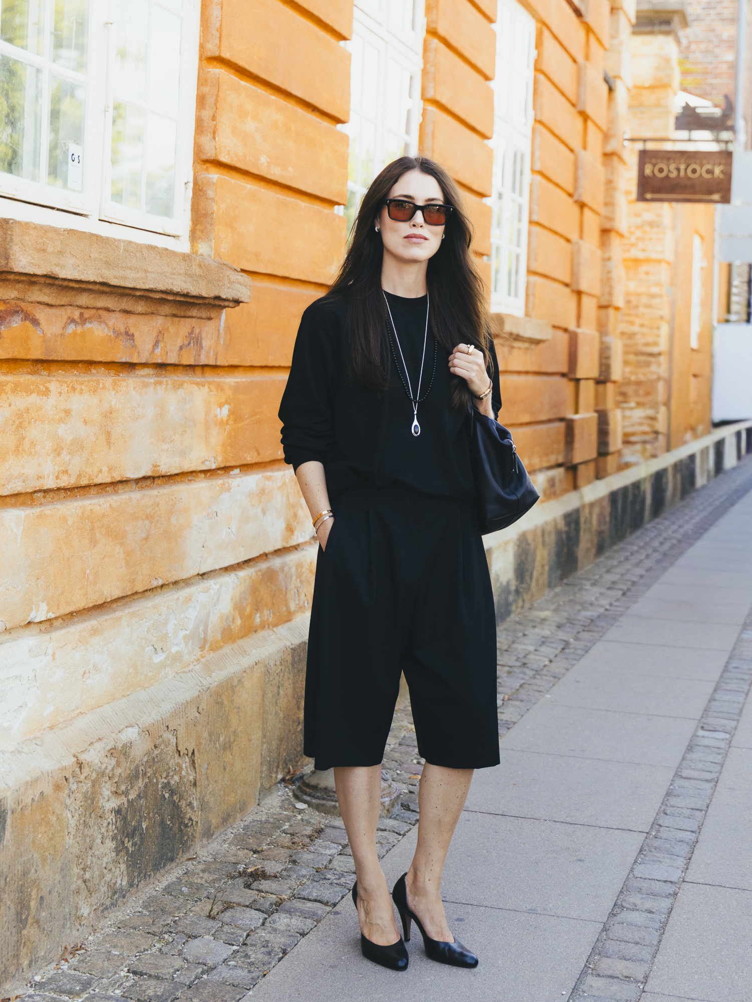 a woman wears black bermuda shorts, black shirt, and black pumps