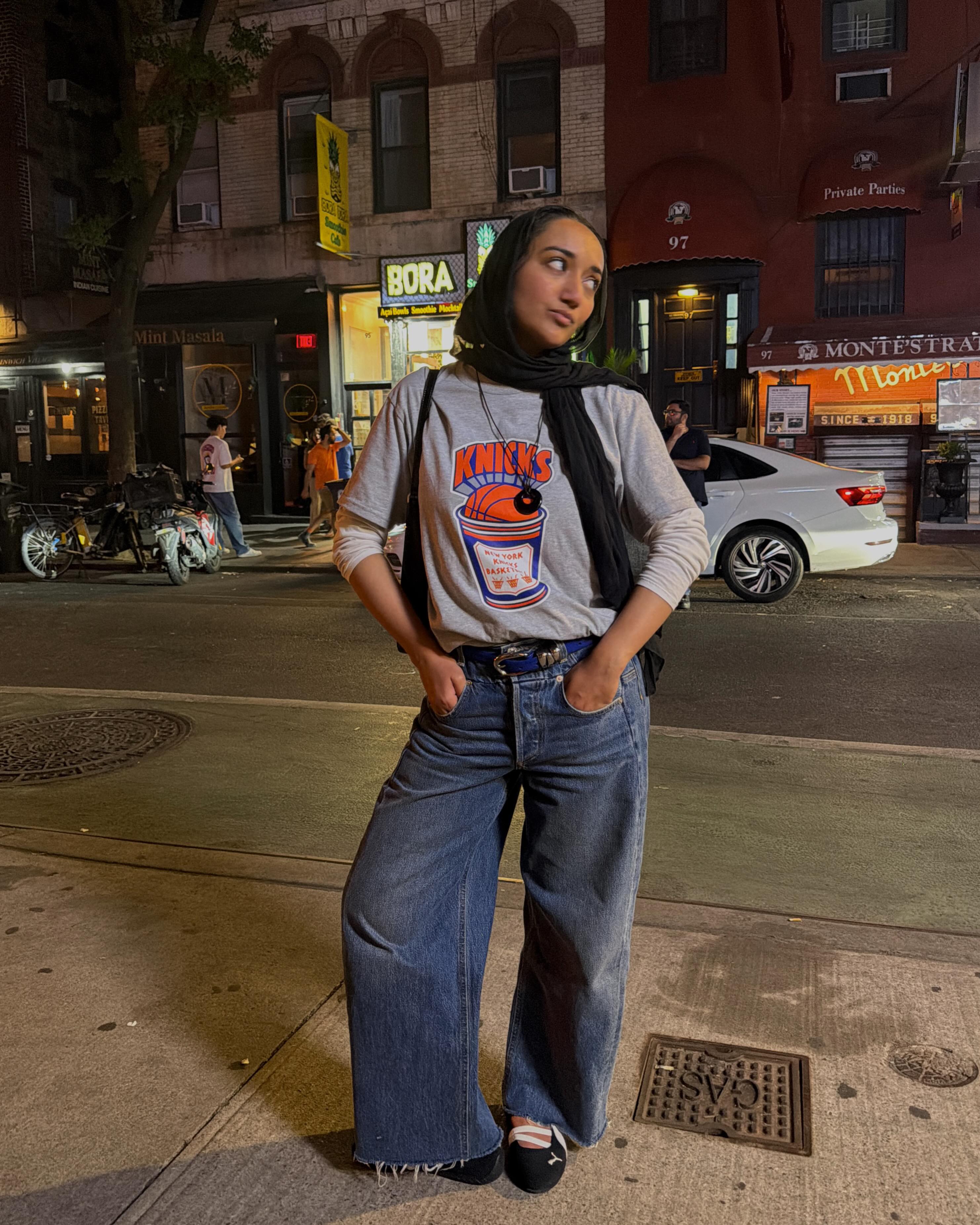 Influencer Yusra Siddiqui wearing a short sleeve t-shirt over a long sleeve t-shirt with wide leg jeans and ballet sneakers.