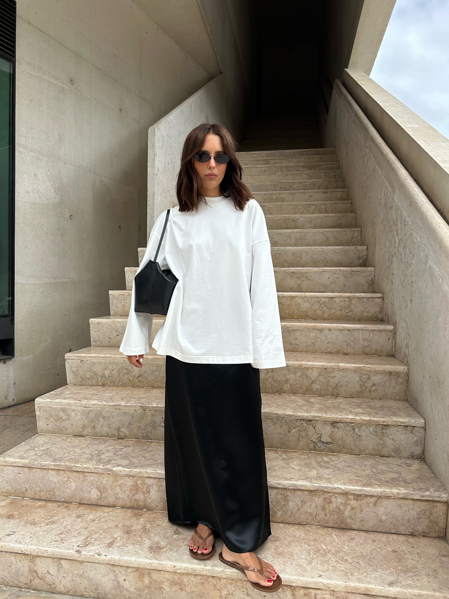 Influencer Debora Brosa wearing a white long sleeve t-shirt, satin skirt and flip flops.