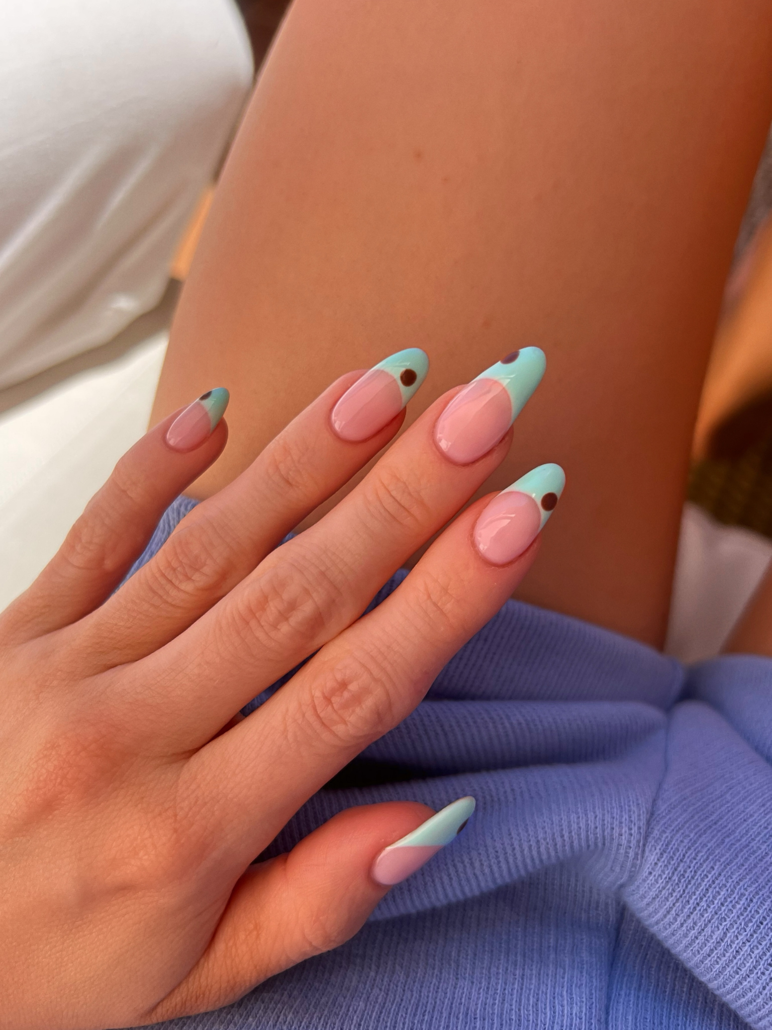 A turquoise French tip nail design with brown dots.