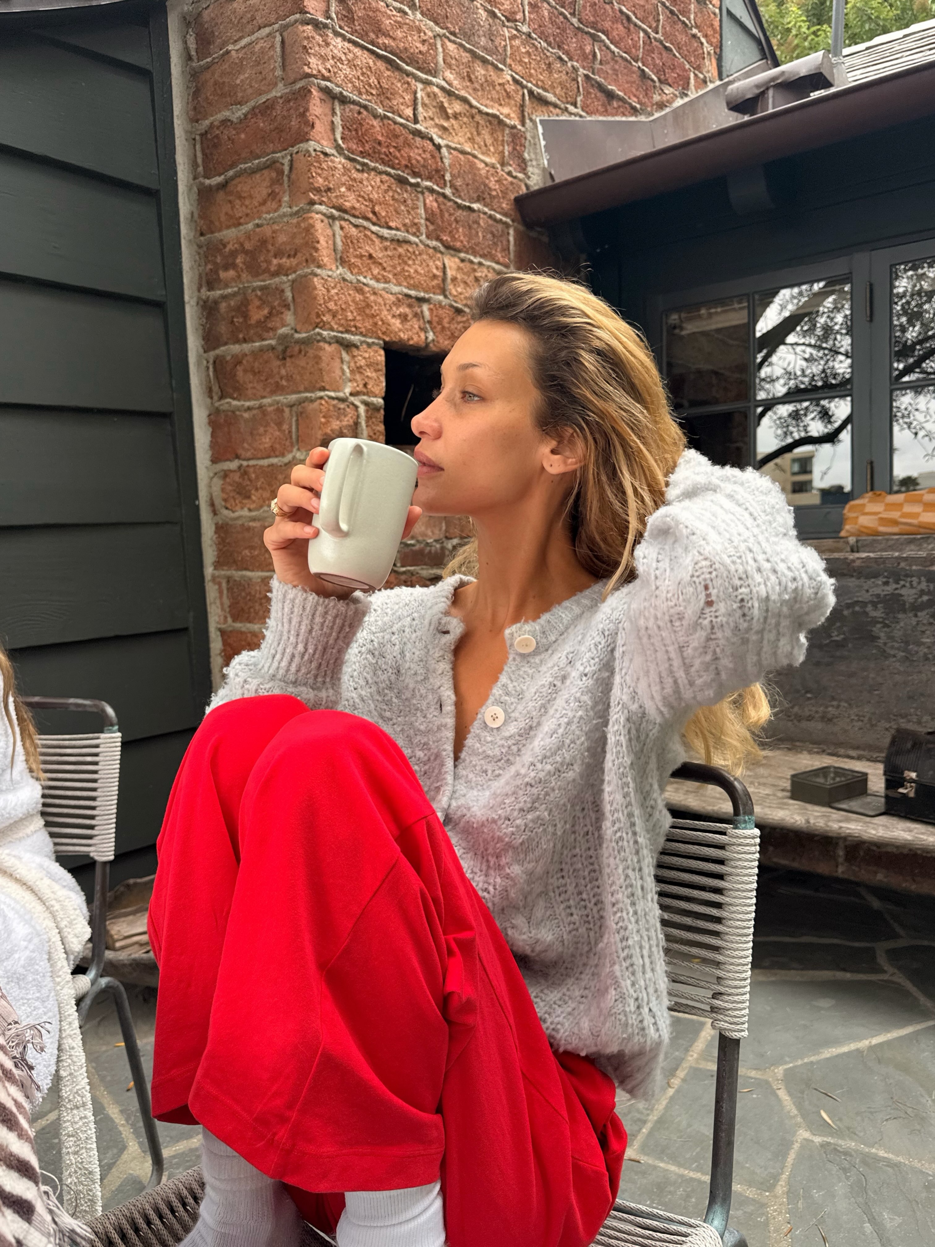 Bella Hadid wears red trousers with a grey fuzzy cardigan.