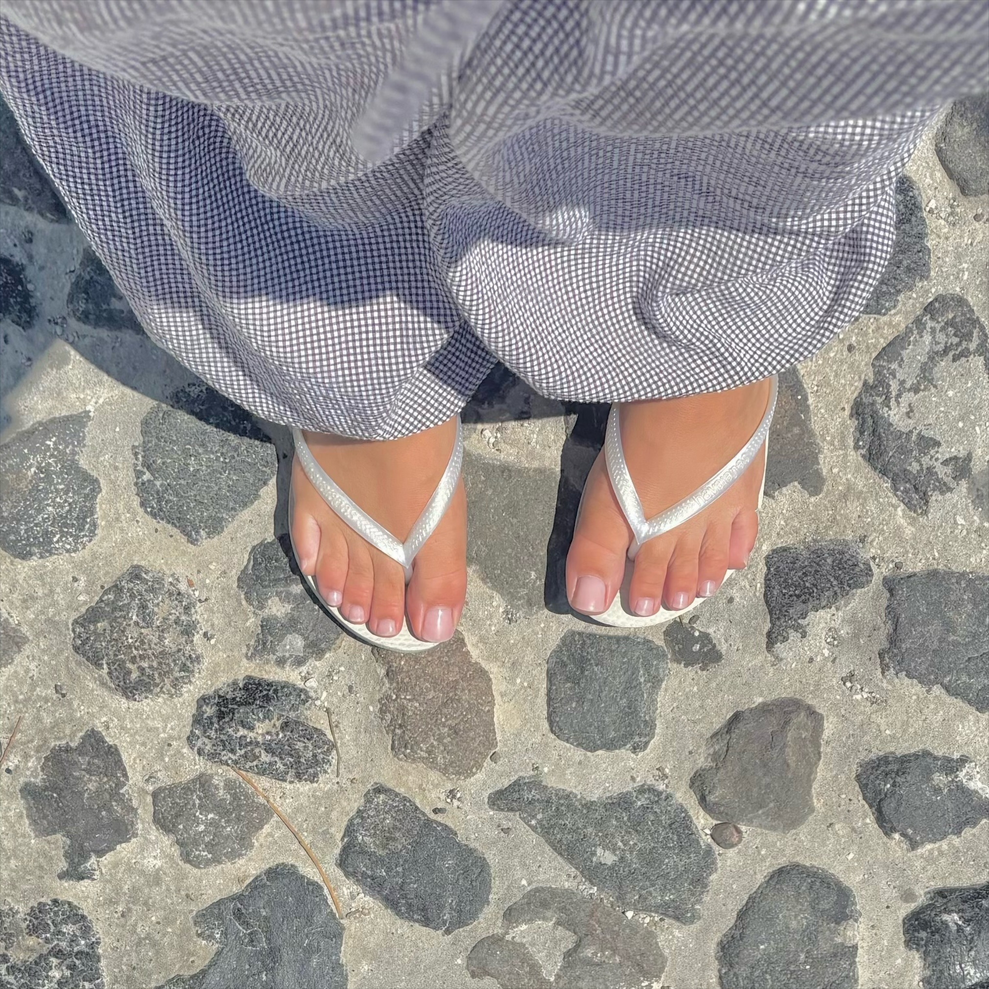 A close-up of feet in white flip flops, toes painted with a natural. pink