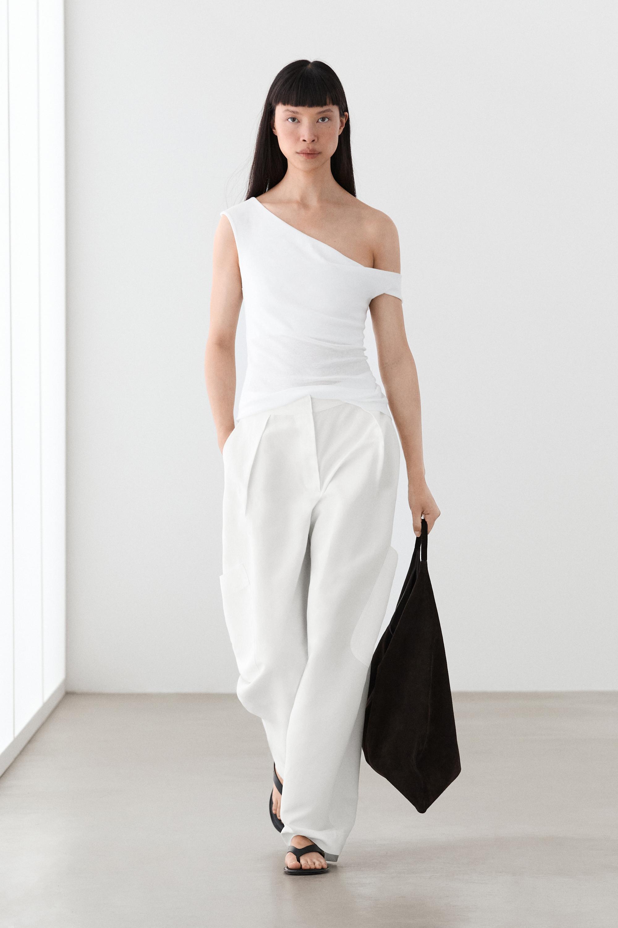 An image of a model wearing a white off shoulder top and white trousers carrying a black bag