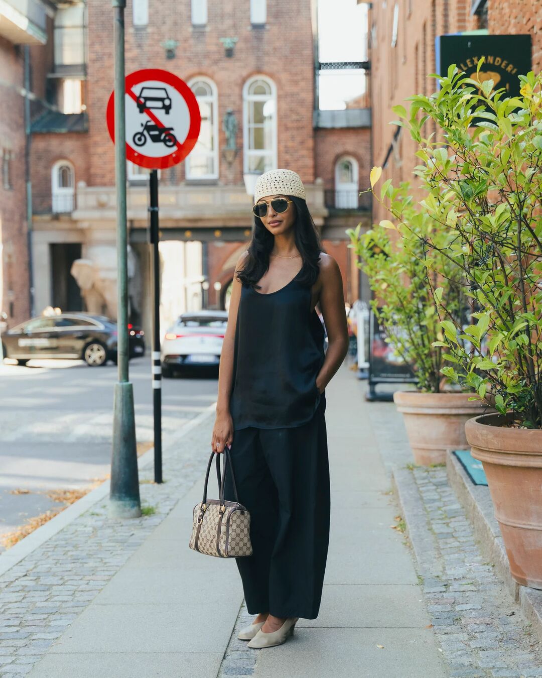 Woman wears black set, luxury handbag, wedges, and skull cap.