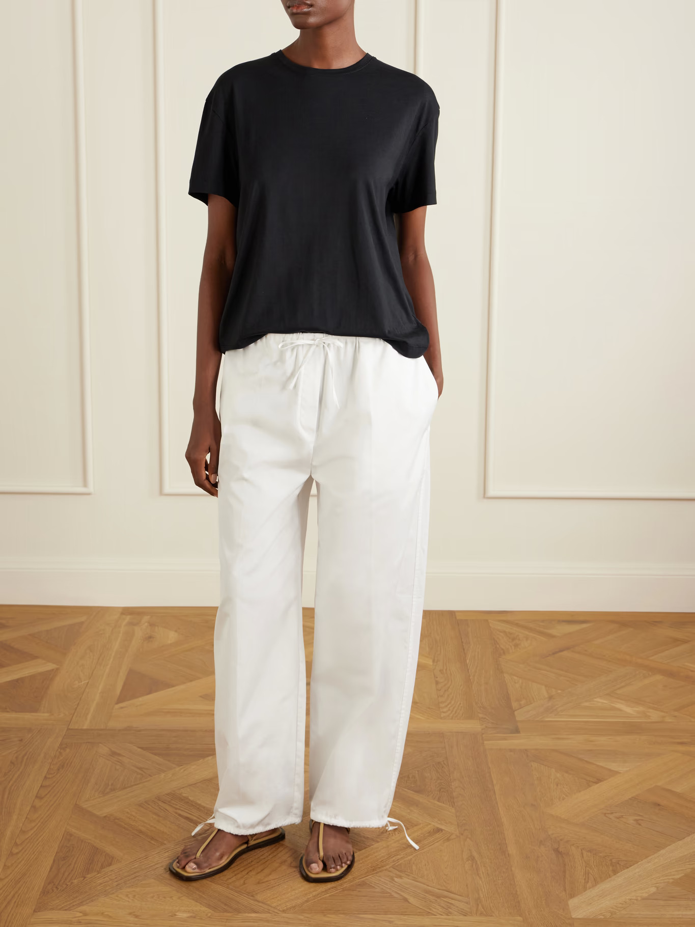 An image of a model wearing white cotton poplin trousers with tie ankles and a black T-shirt