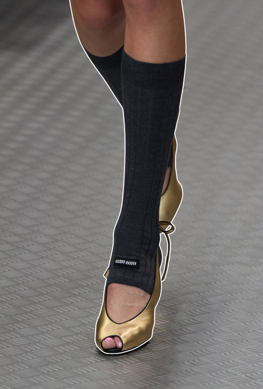 Image from the Miu Miu SS 2025 runway show the model wears peep toe heels with the toeless sock trend. She wears a calf-lenght grey pair from Miu Miu.