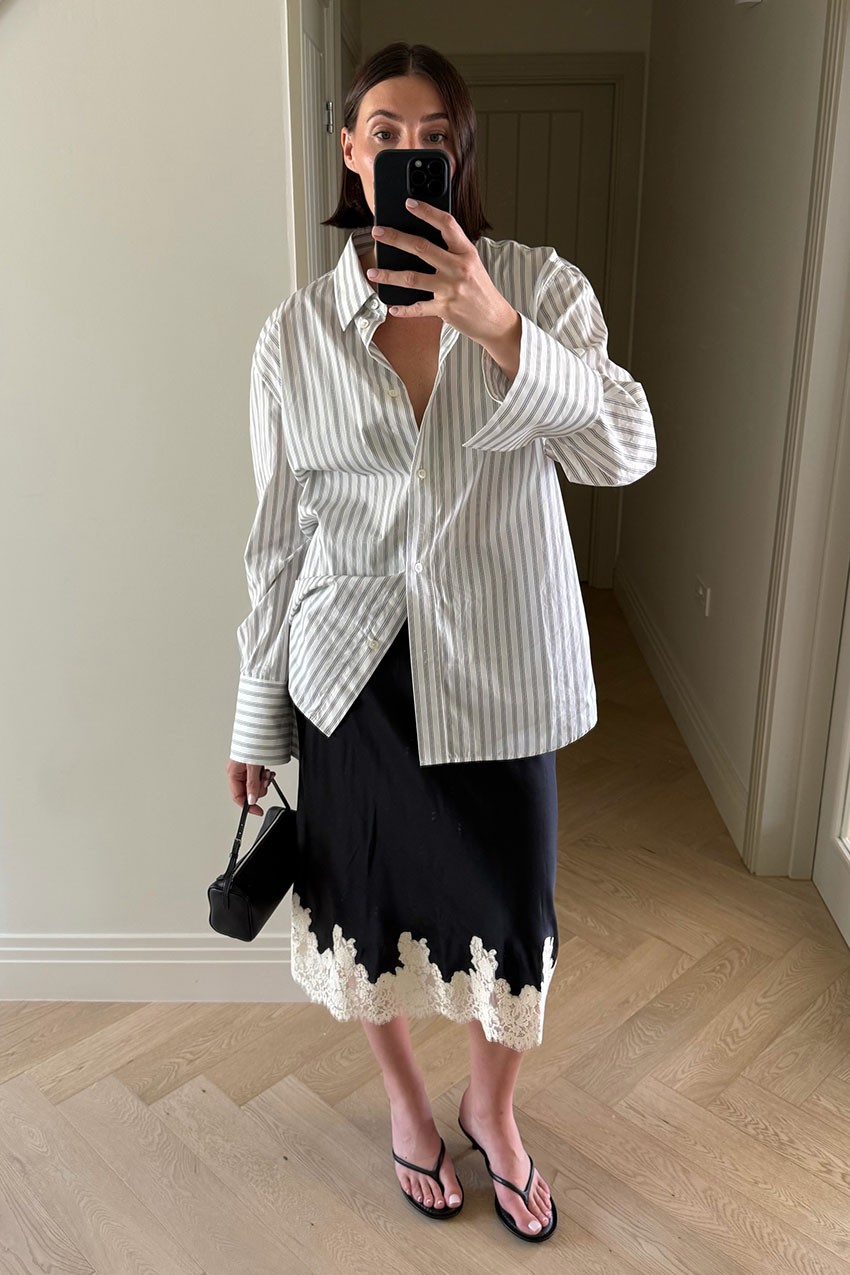 A woman wearing a button-down, black lace-trim skirt, and flip-flops.