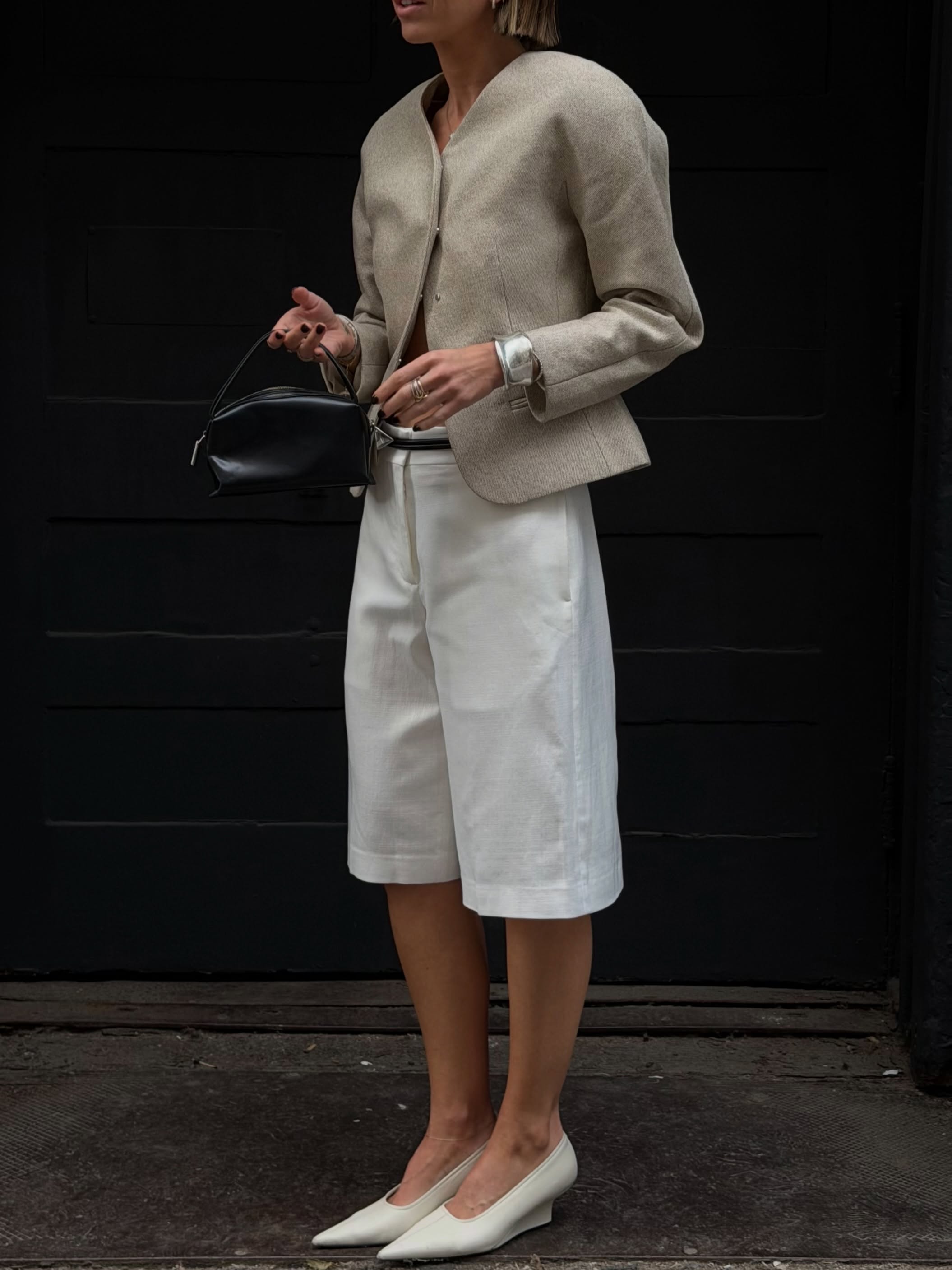 An image of an influencer wearing a beige structured blazer, white Bermuda shorts and white micro wedge heels in New York City