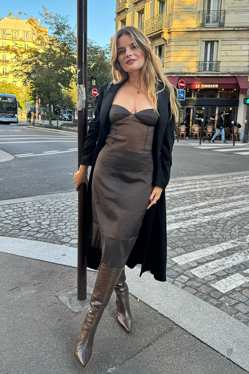 a woman wearing a brown dress, black coat, and brown knee-high boots