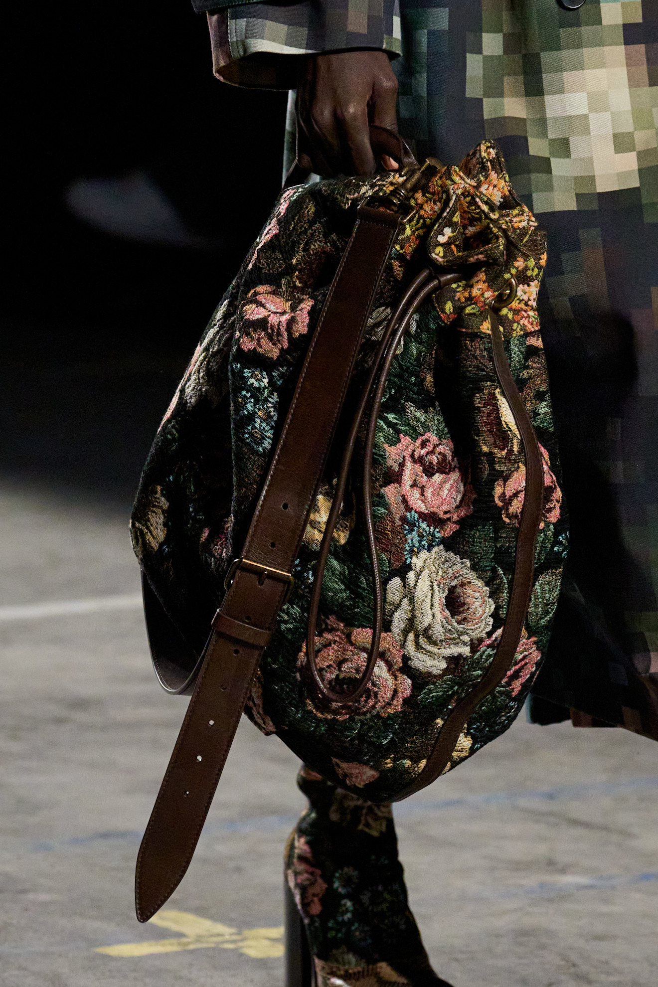 A closeup image of a Dries Van Noten model carrying a carpet floral tote with a brown leather strap from the autumn 2026 runway.