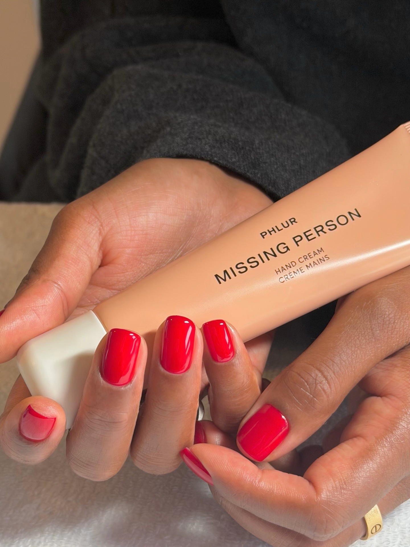 A woman holding a Phlur hand cream with a bright red manicure