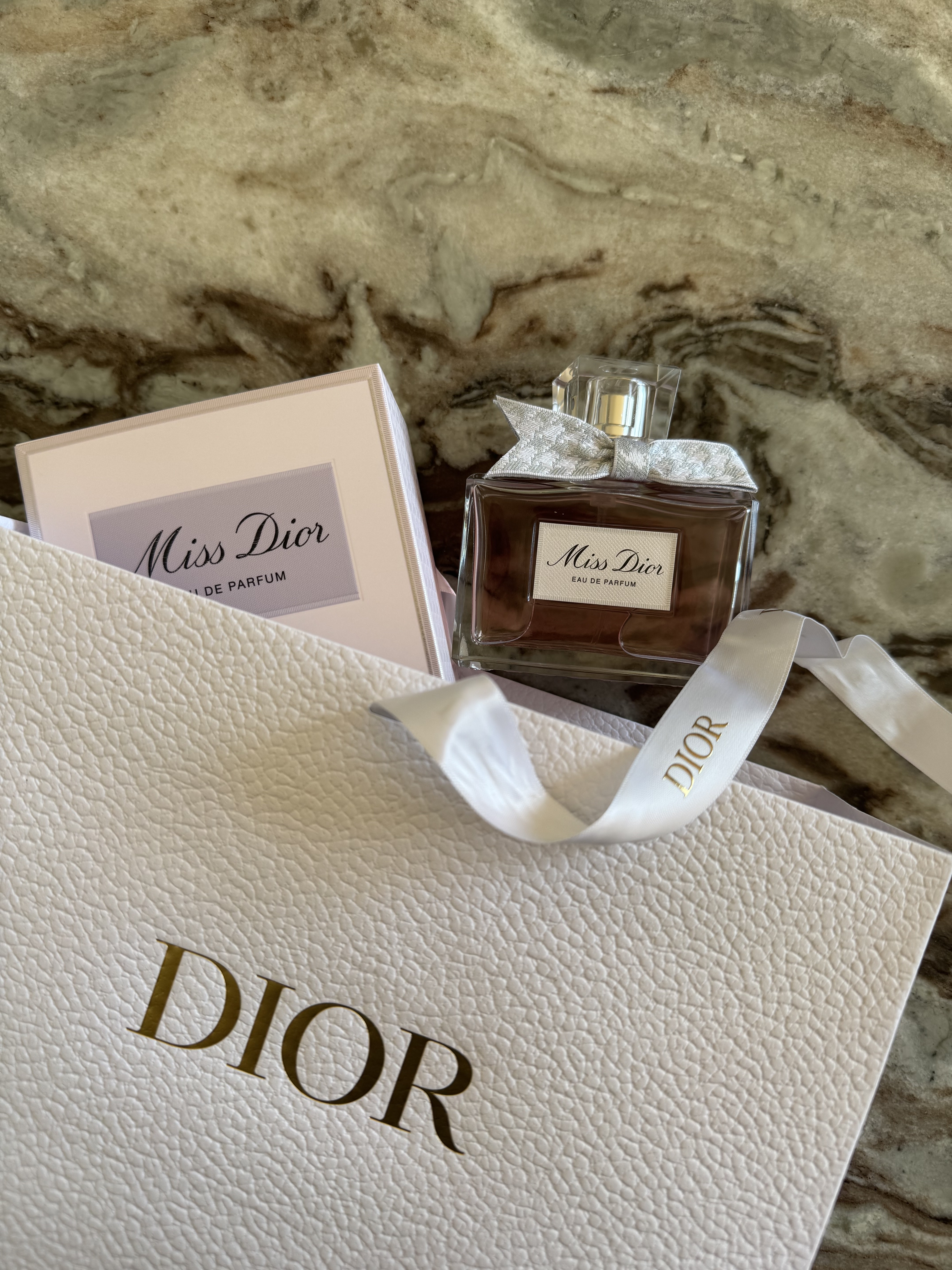 A dior perfume bottle peeking out from a dior paper bag