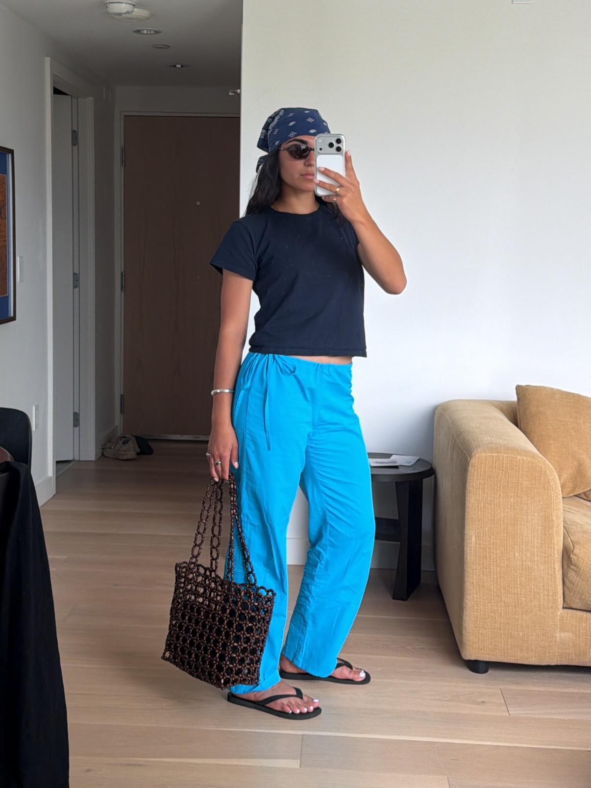 An image of an influencer taking a mirror selfie wearing a blue bandana, navy blue T-shirt, aqua tie-waist cotton poplin trousers and black flip-flops