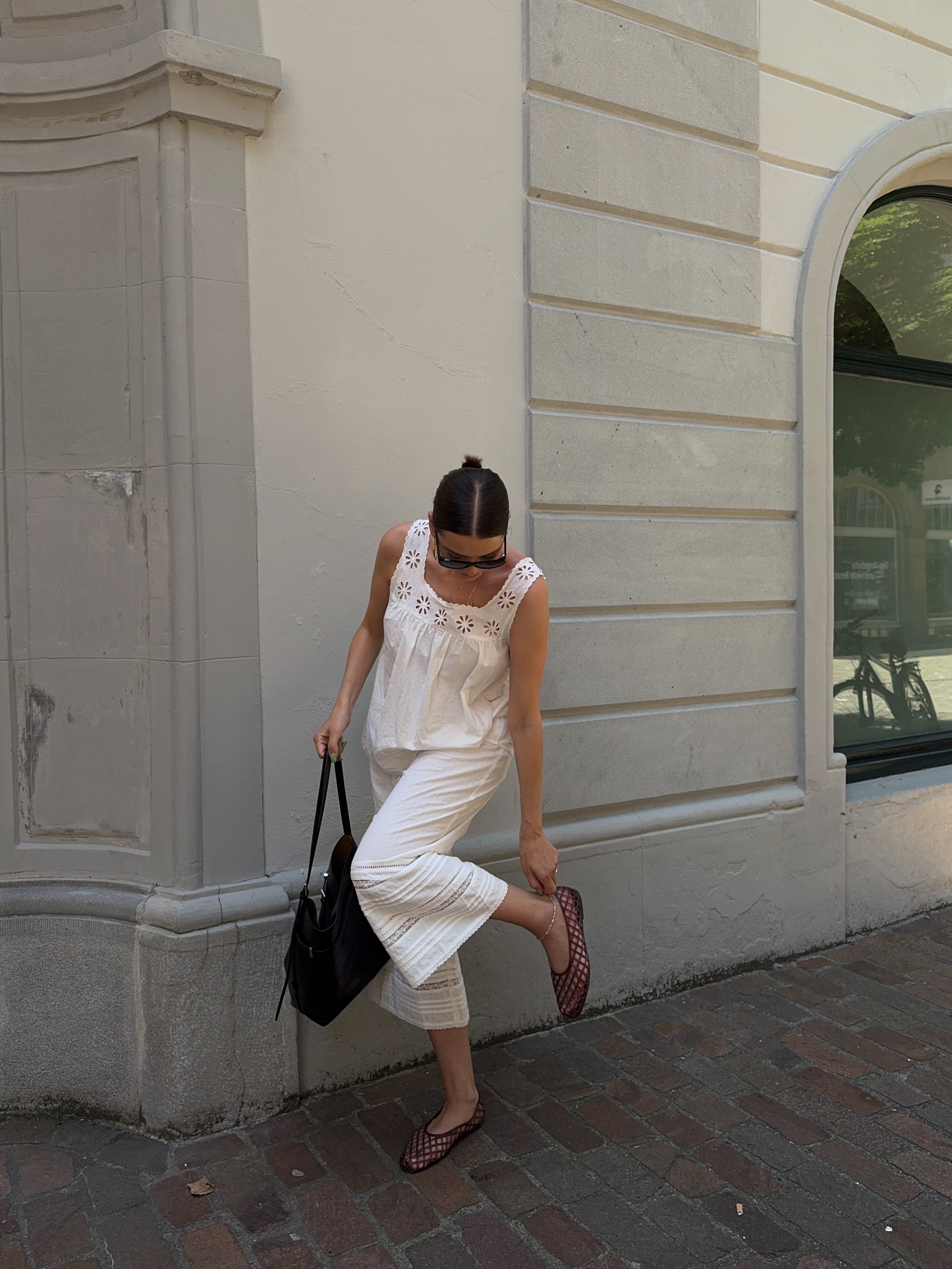 An image of an influencer in white lace capris and a sleeveless white lace top with burgundy mesh ballet flats