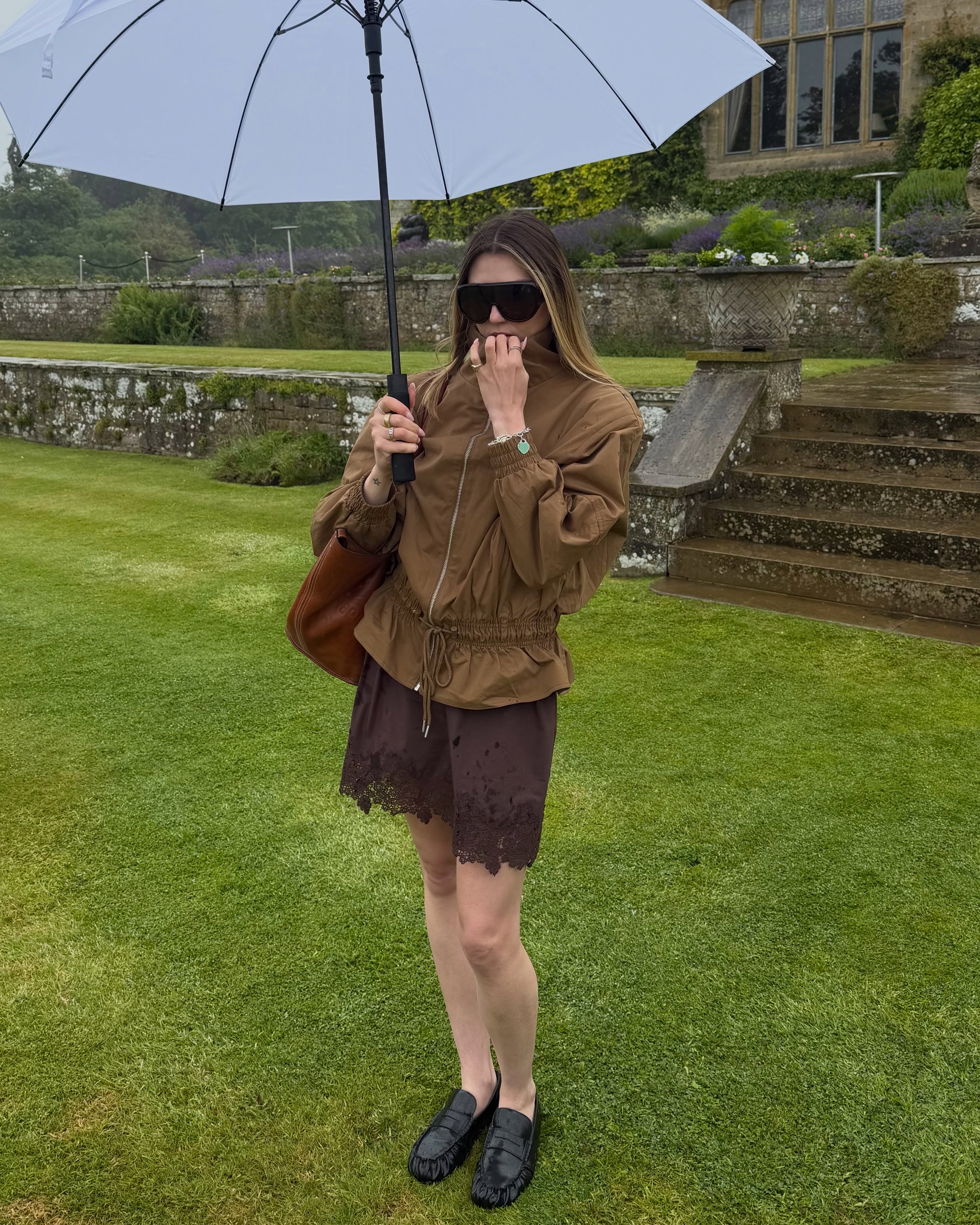 Influencer Lou Northcote wearing a brown technical jacket and lace-hem shorts with loafers and sunglasses.