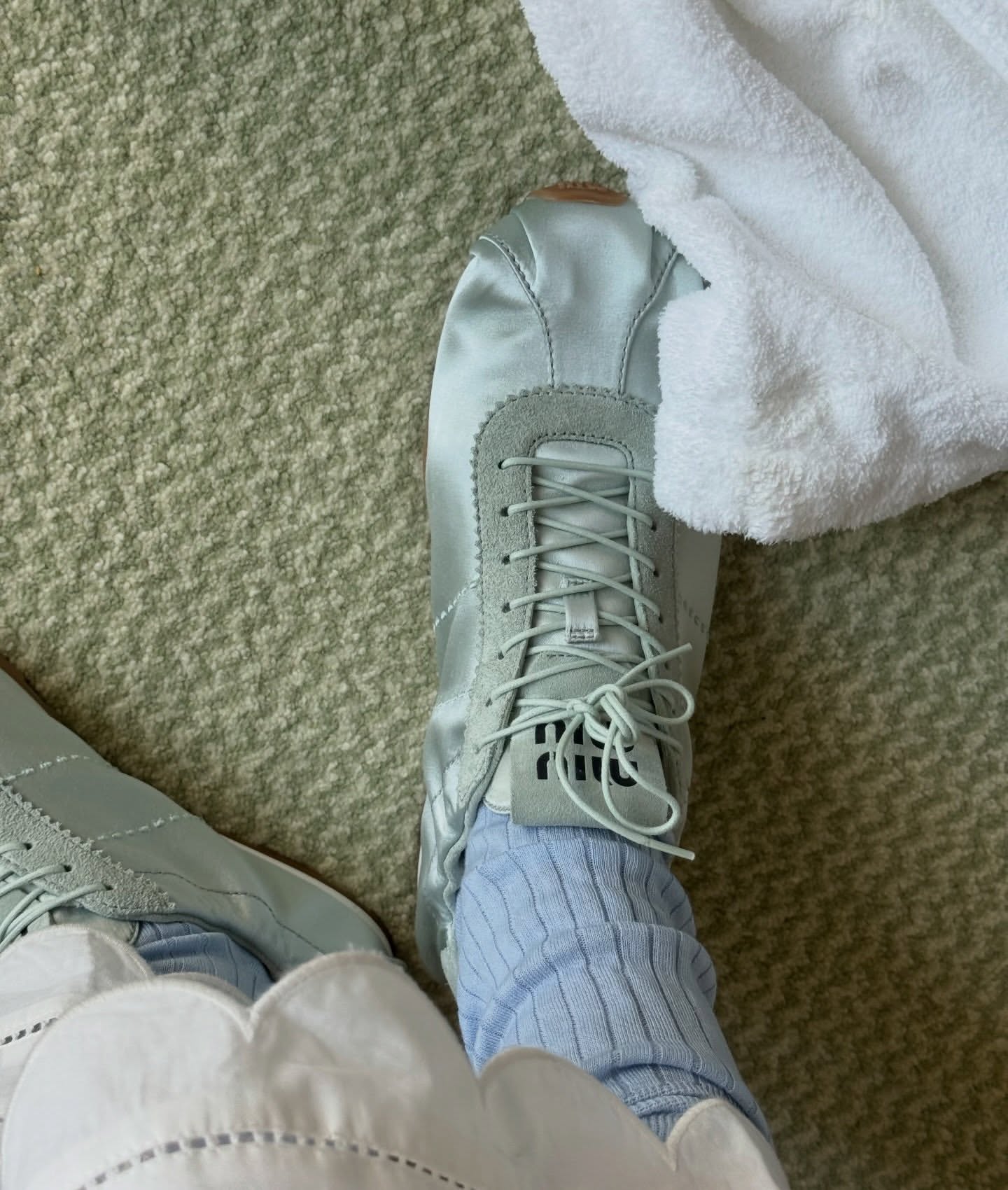 A closeup image of an influencer's mint green satin Miu Miu trainers with light blue socks and white scallop-hem trousers