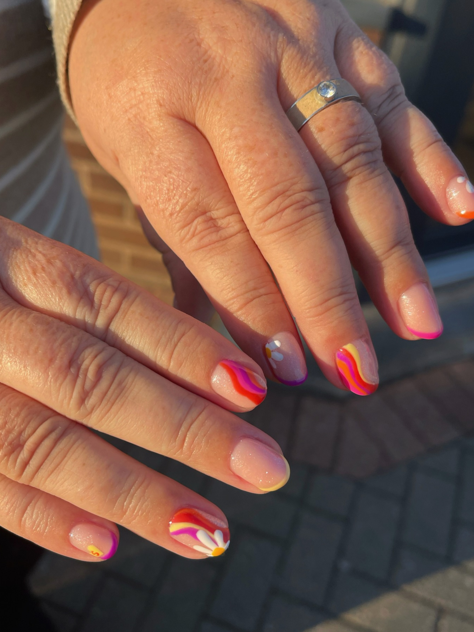 Nails with a wavy design in bright pink, red, and yellow.