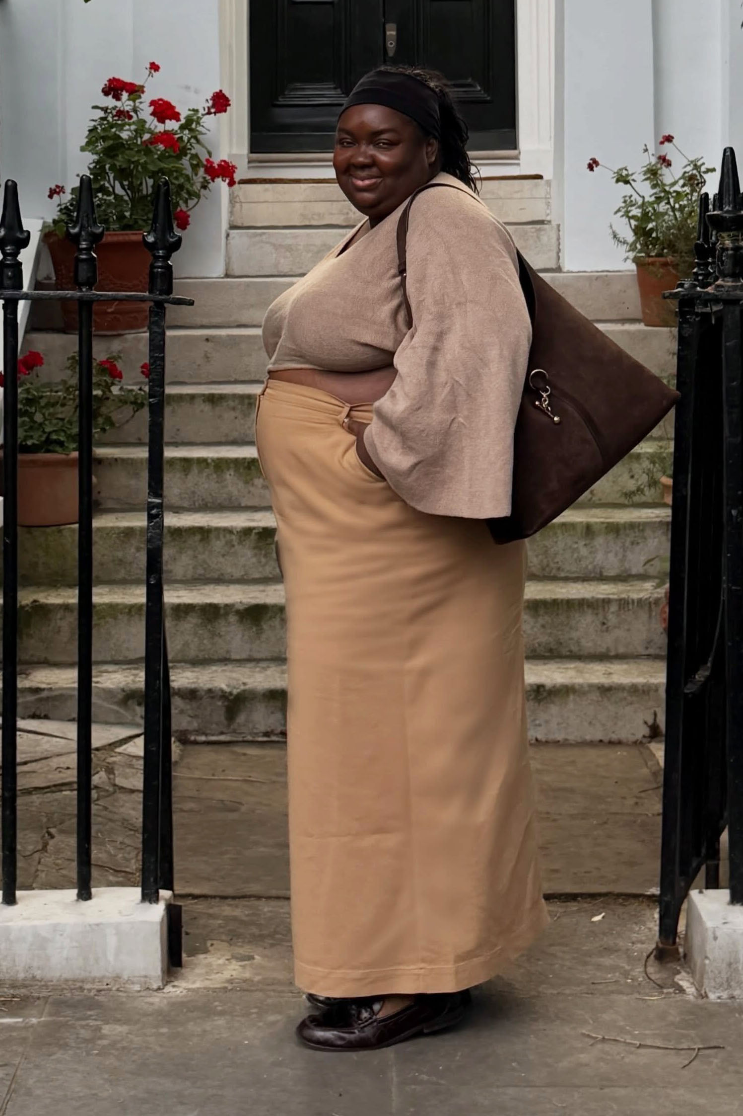 a woman wearing a tan top, tan long skirt, black flats, and brown bag