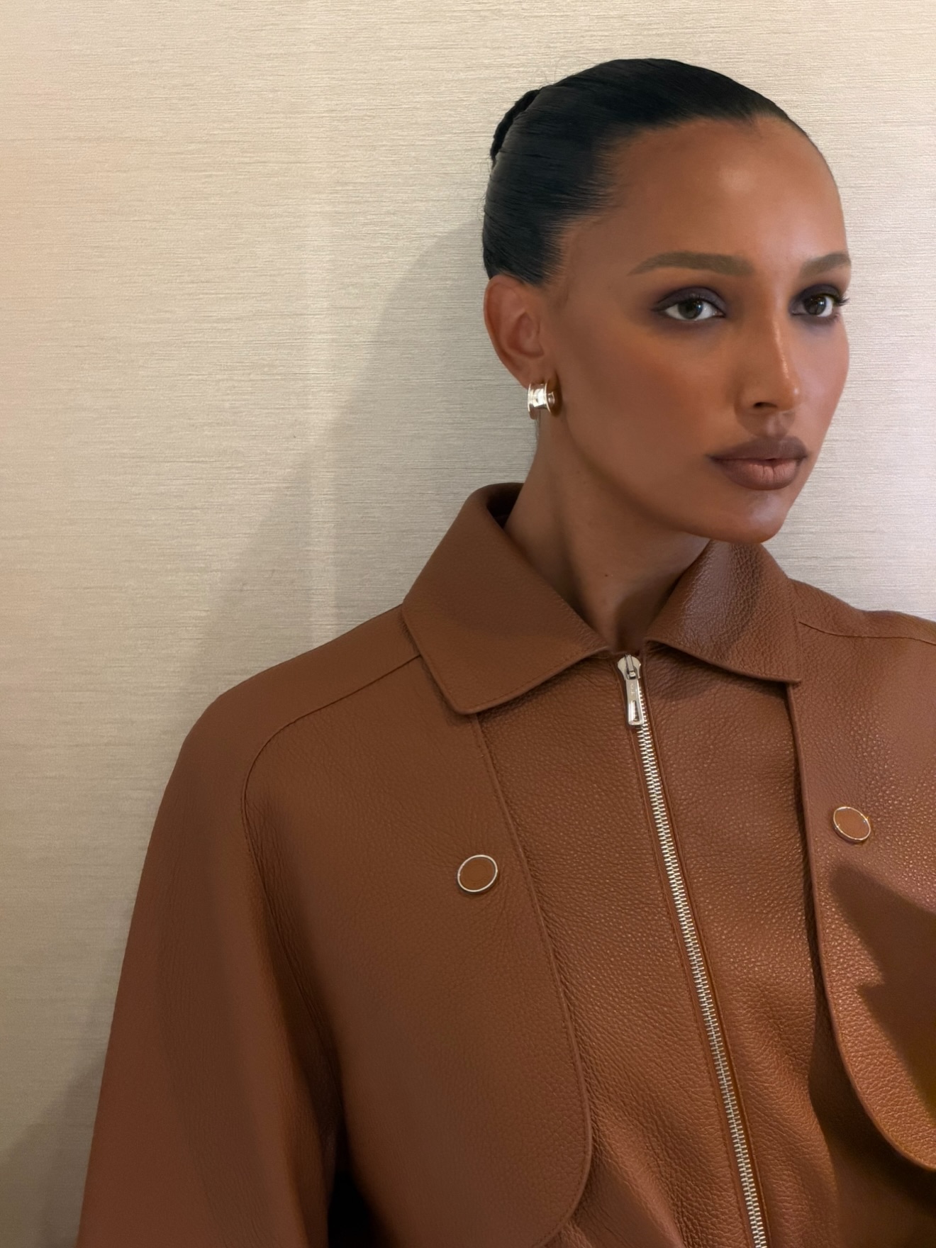Photo of Jasmine Tookes wearing a brown jacket with hair slicked back into a bun