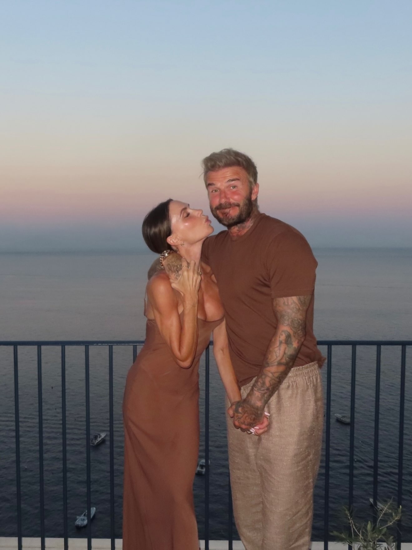 Victoria Beckham poses for a photo with David Beckham wearing a dark brown slip dress.