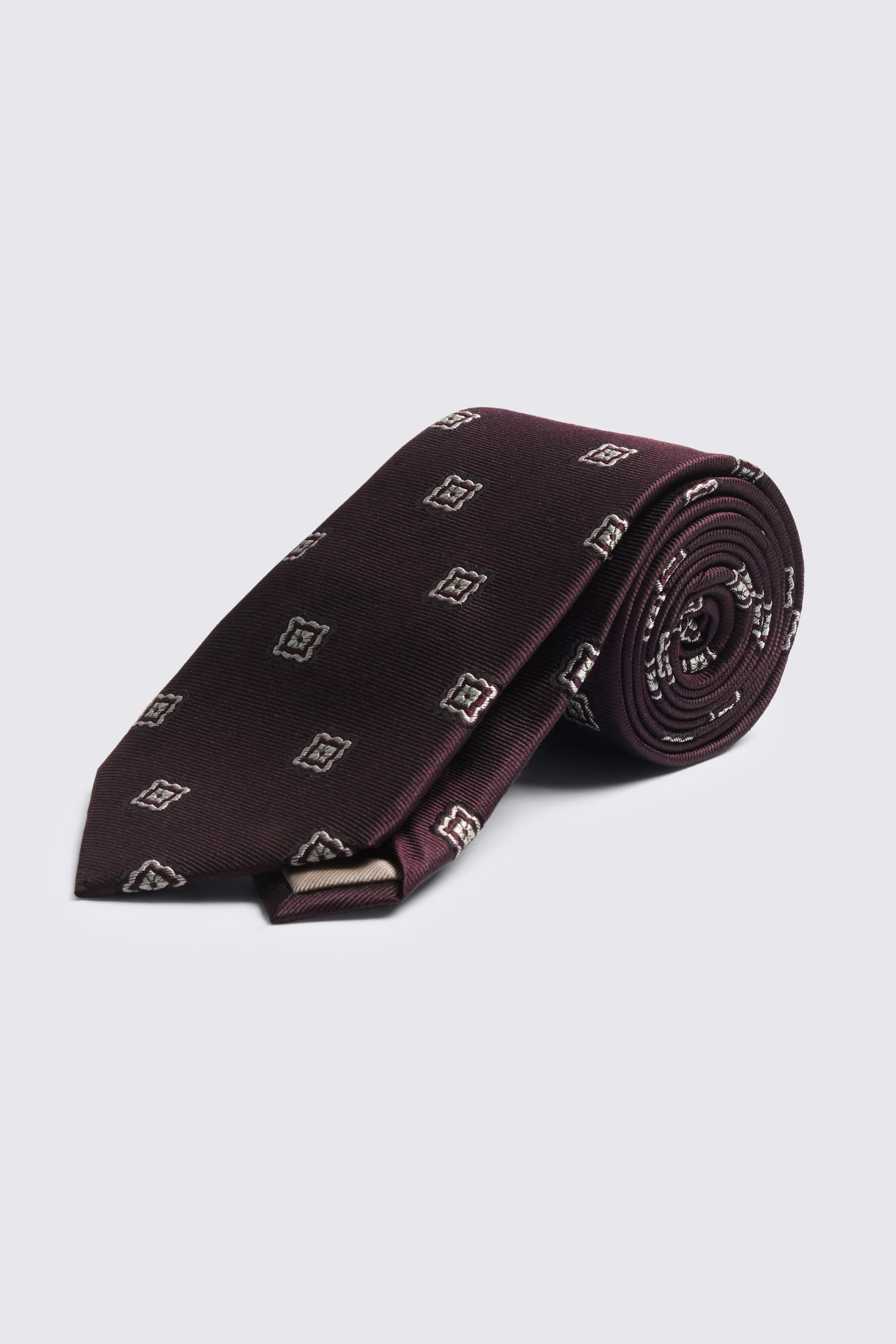 An image of a dark purple tie rolled up with a silver medallion pattern