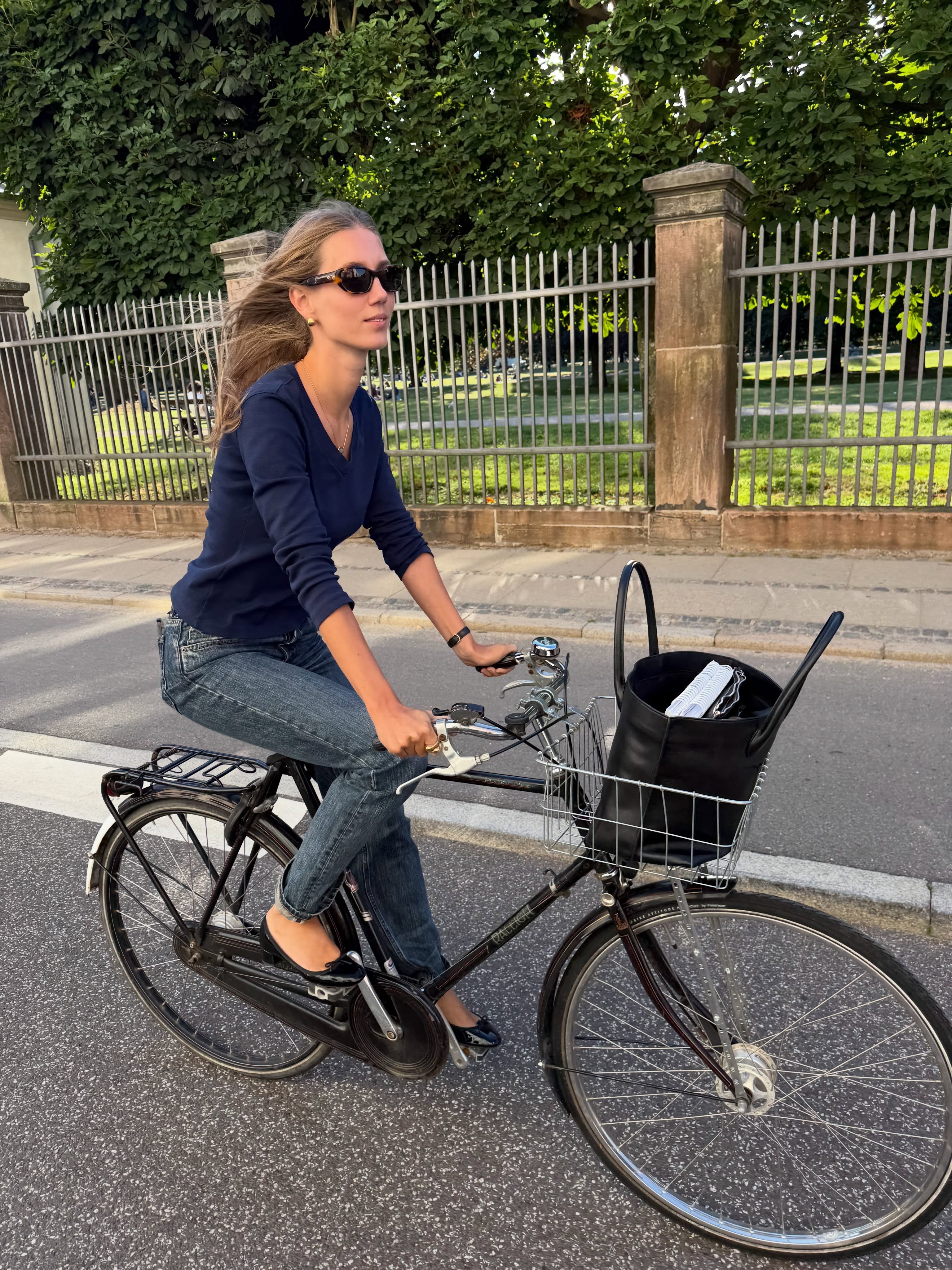 Influencer @amaliemoosgaard rides a bike wearing a v-neck knit with skinny jeans and black ballet flats.